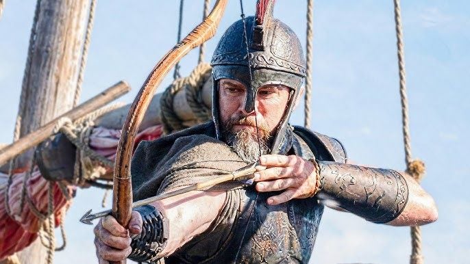 Ein Krieger in Rüstung zieht einen Bogen auf einem antiken Schiff, bereit zu schießen.