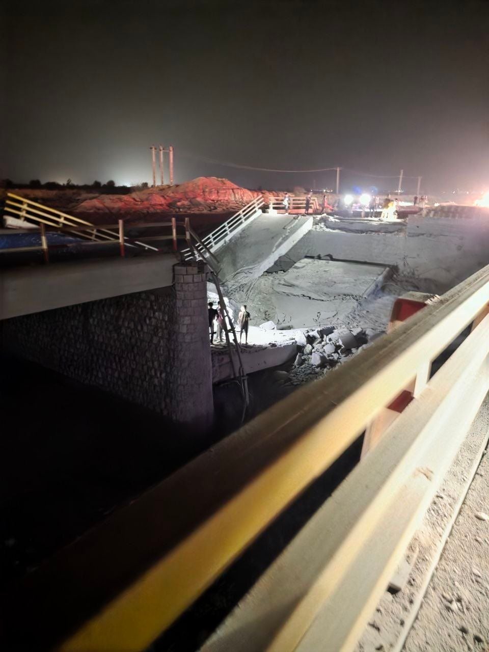 Eingestürzte Brücke bei Nacht mit Rettungskräften und Baustellenbeleuchtung in Iran.