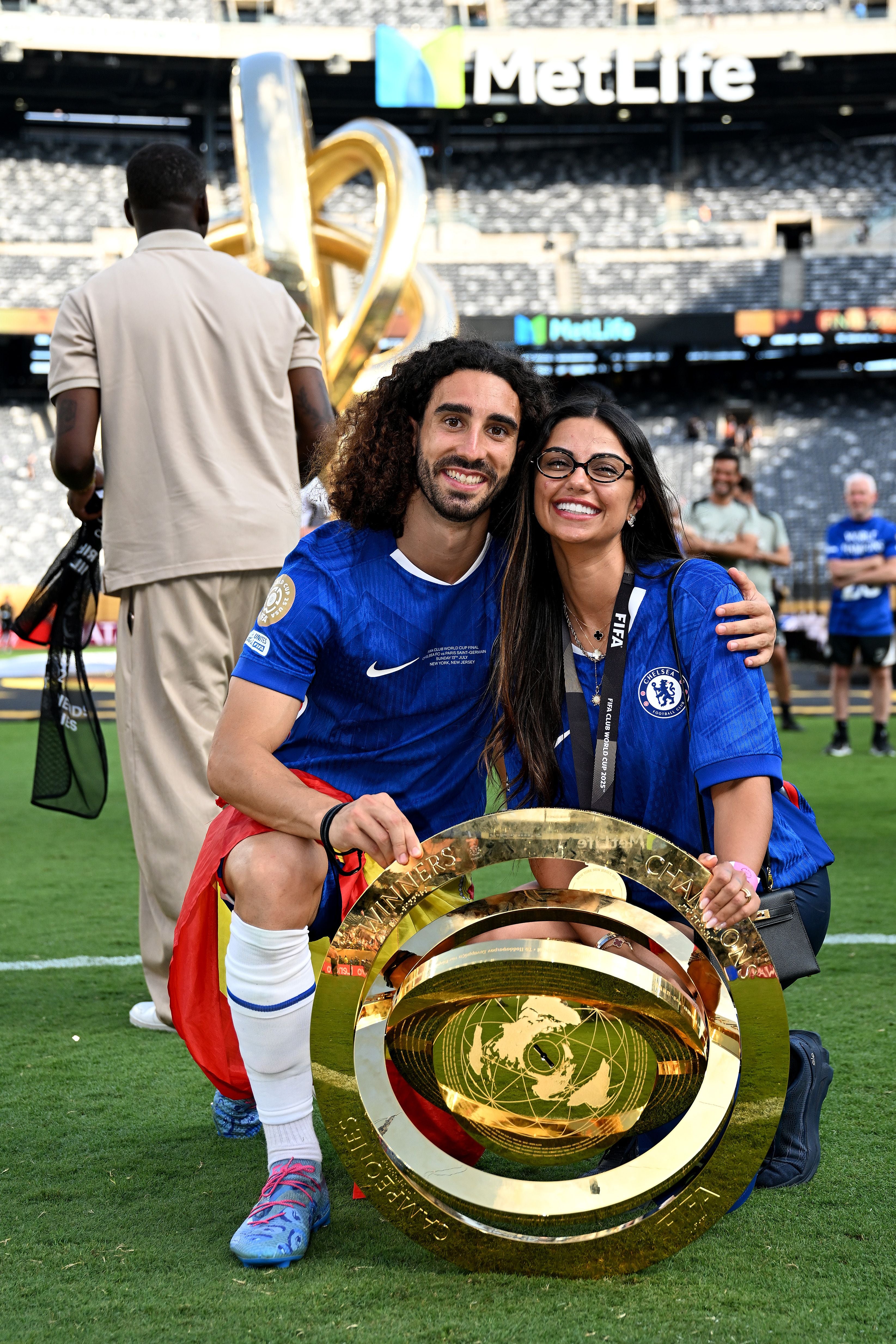 Ein Fußballspieler und eine Frau posieren mit einem großen goldenen Pokal im Stadion.