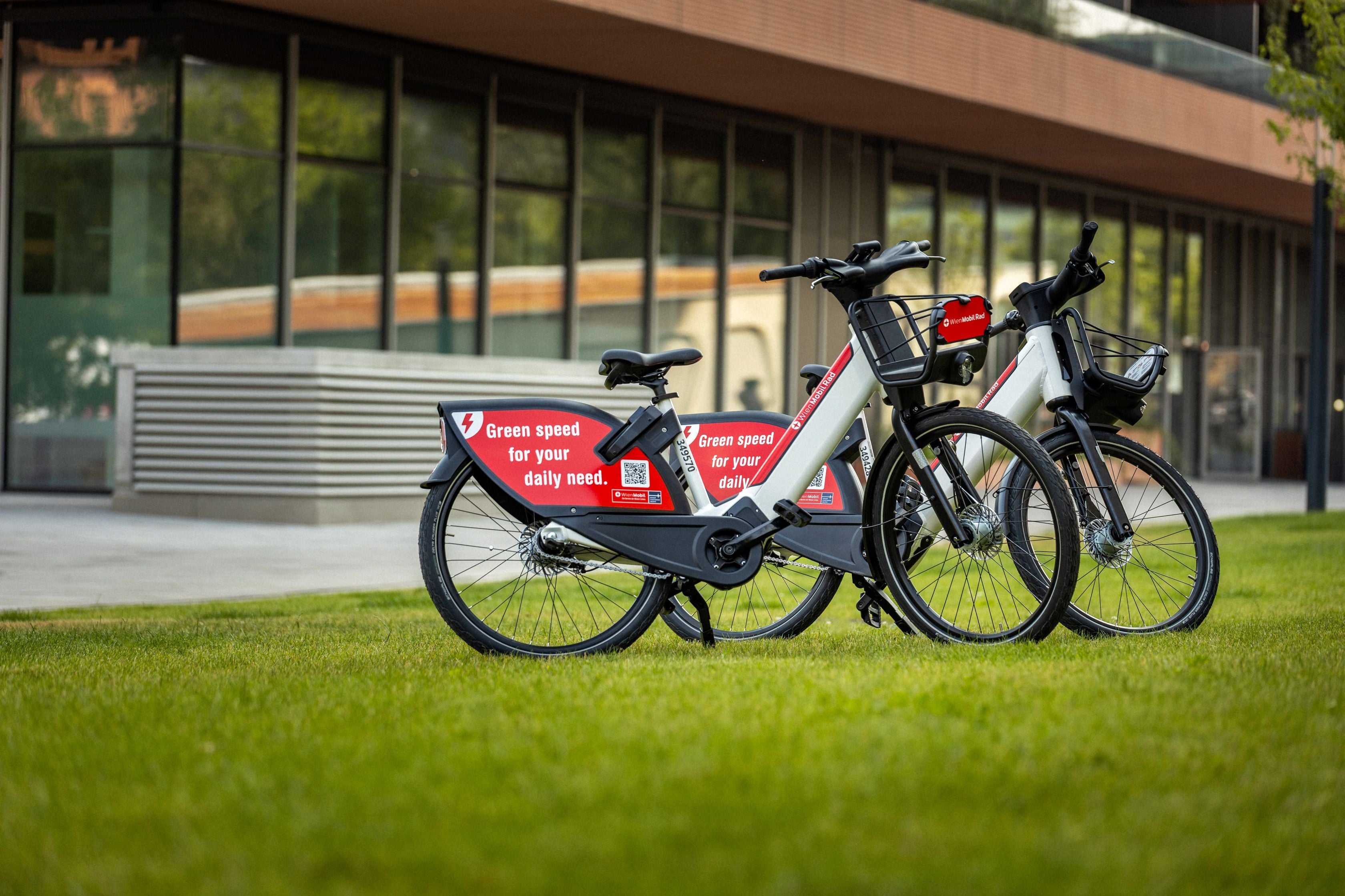 Zwei E-Bikes stehen auf einer Wiese vor einem modernen Gebäude.