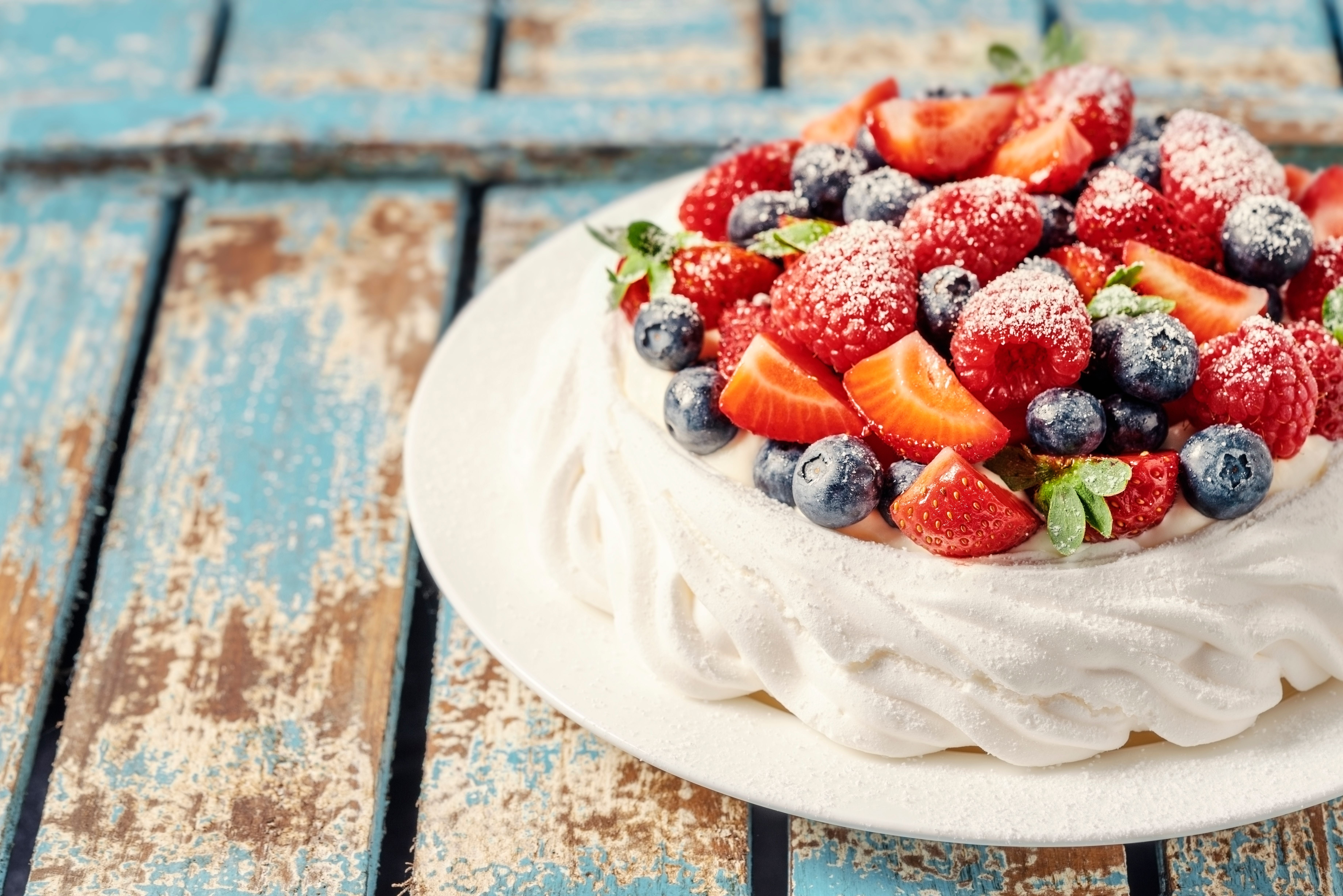 Pavlova-Torte mit Erdbeeren, Himbeeren und Heidelbeeren, bestäubt mit Puderzucker.