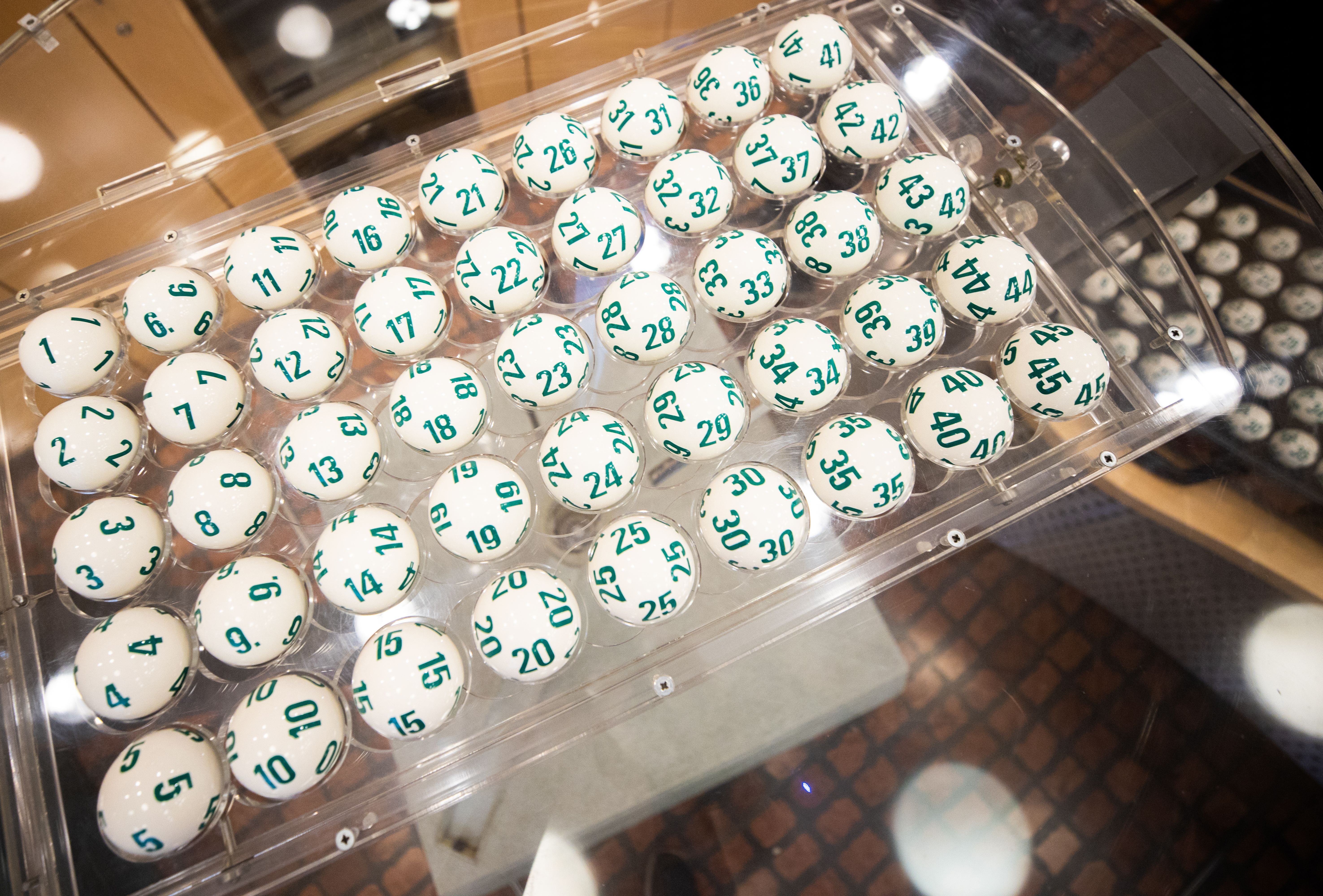Mehrere nummerierte Lottokugeln liegen gestapelt in einer transparenten Lotto-Ziehungsmaschine.