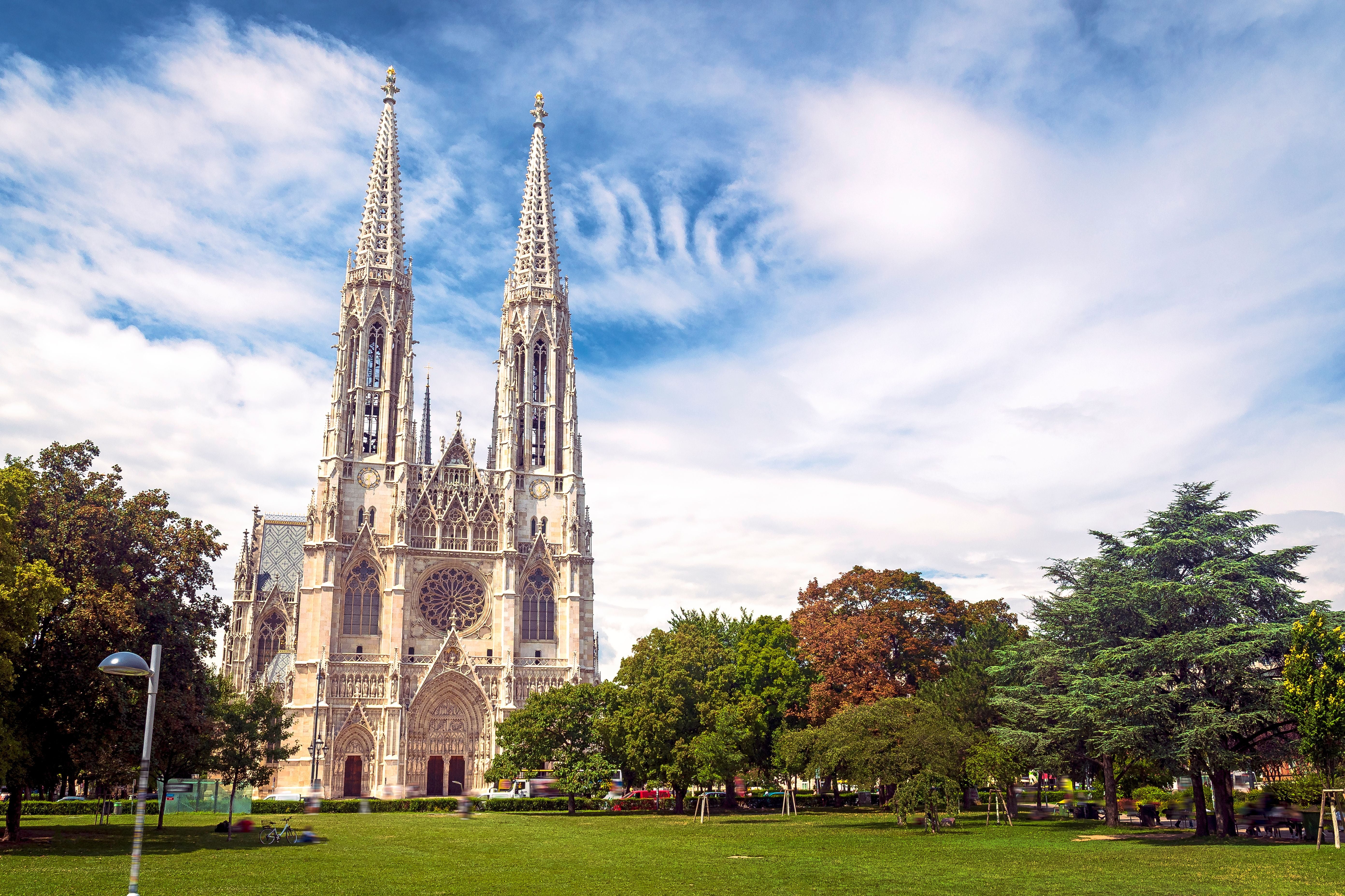 Die neugotische Votivkirche in Wien mit zwei hohen Türmen hinter einer grünen Parklandschaft.