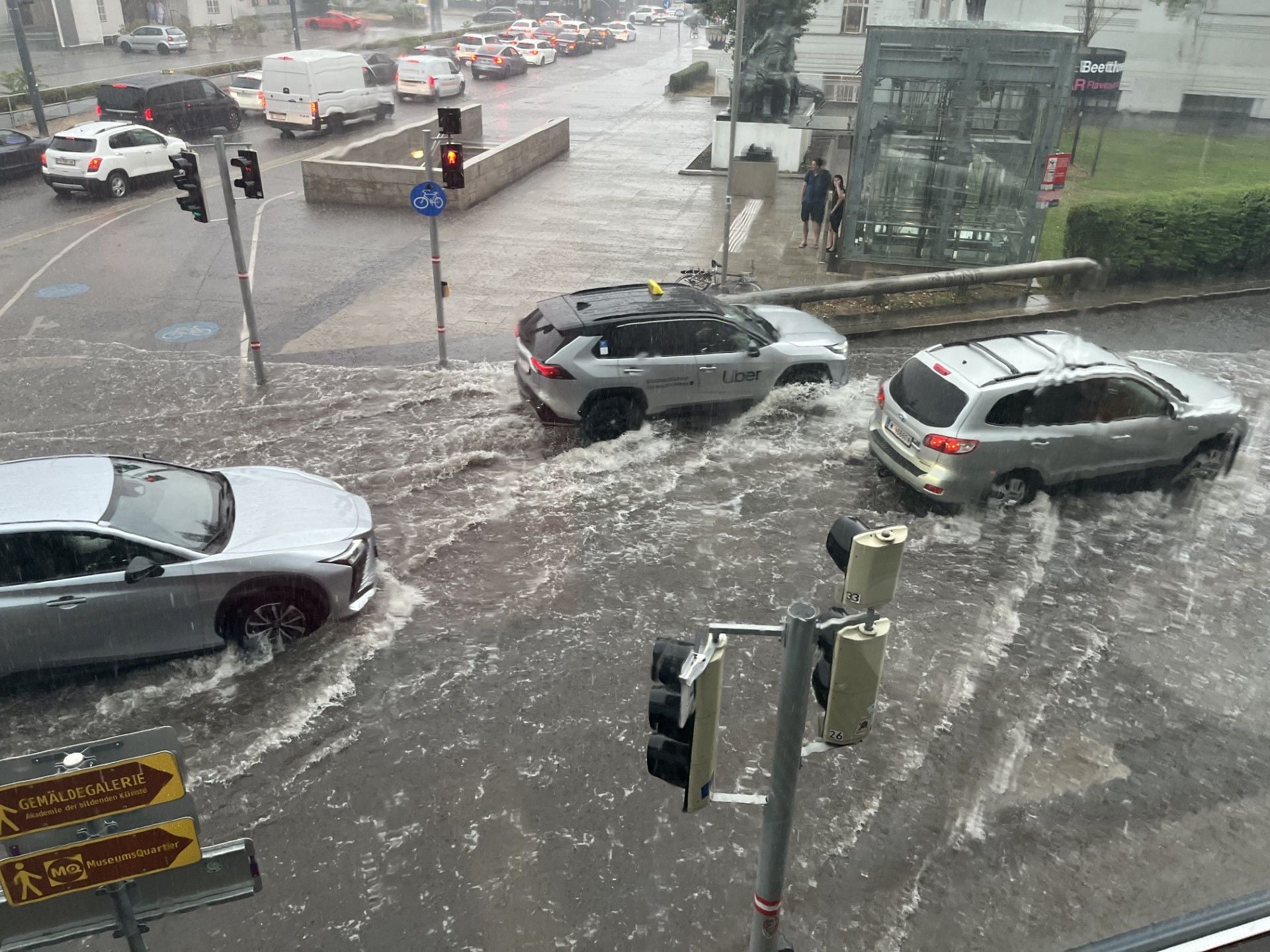 Autos fahren durch überflutete Straßen bei starkem Regen am Karlsplatz, Wien.