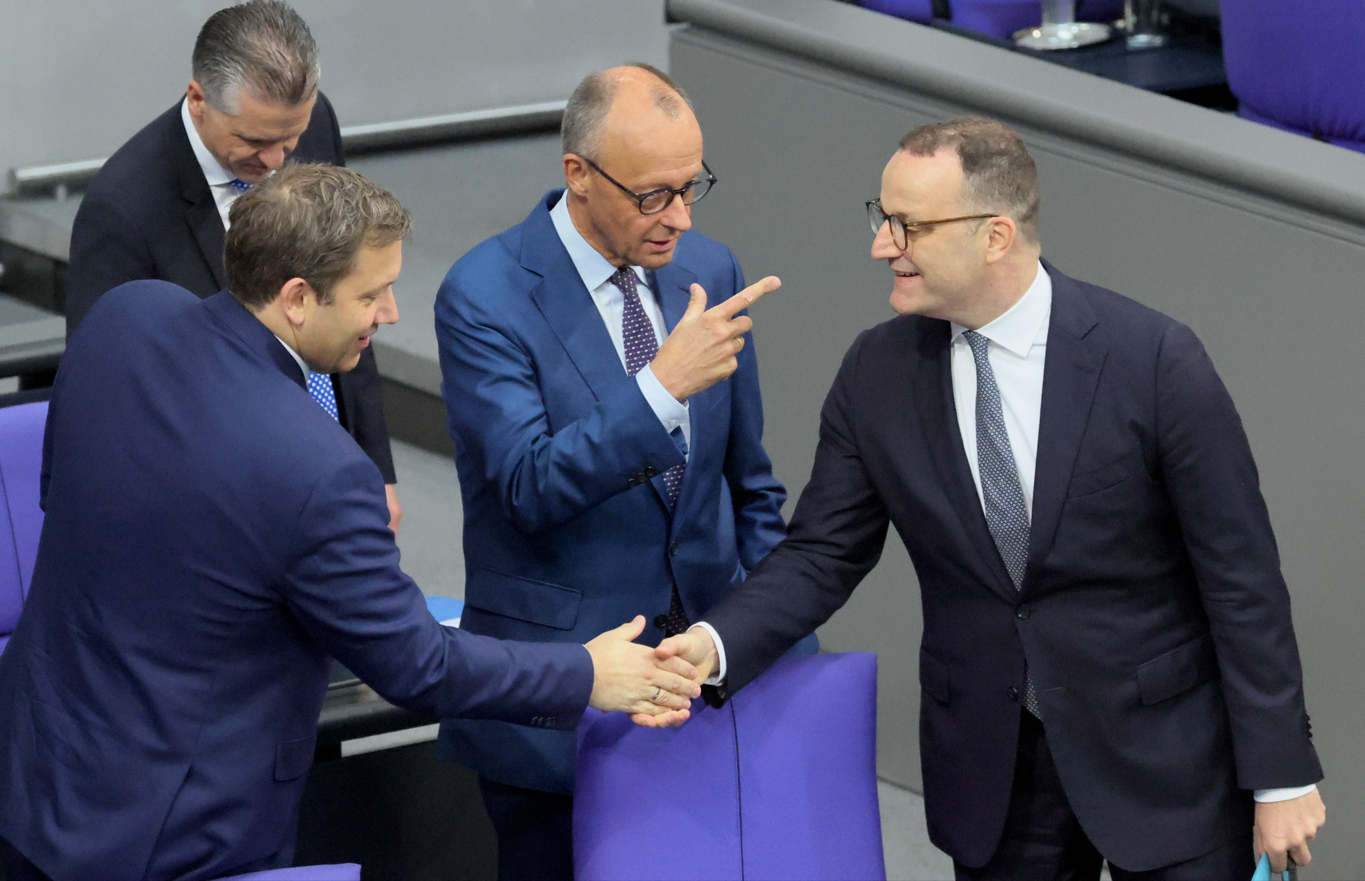 Drei Männer im Anzug unterhalten sich und geben sich im Bundestag die Hand.