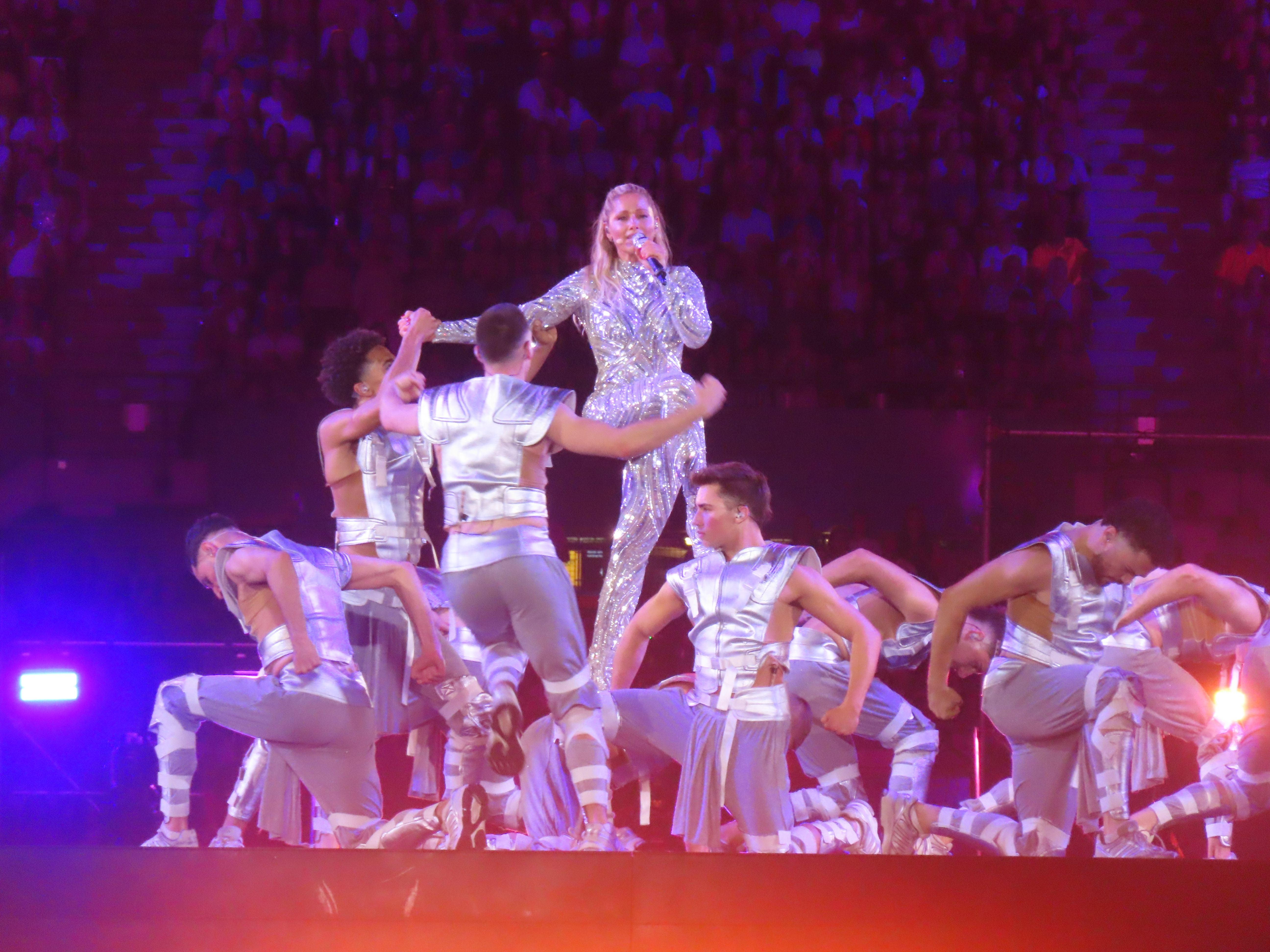 Helene Fischer tritt mit Tänzern in silbernen Outfits auf einer Bühne auf.