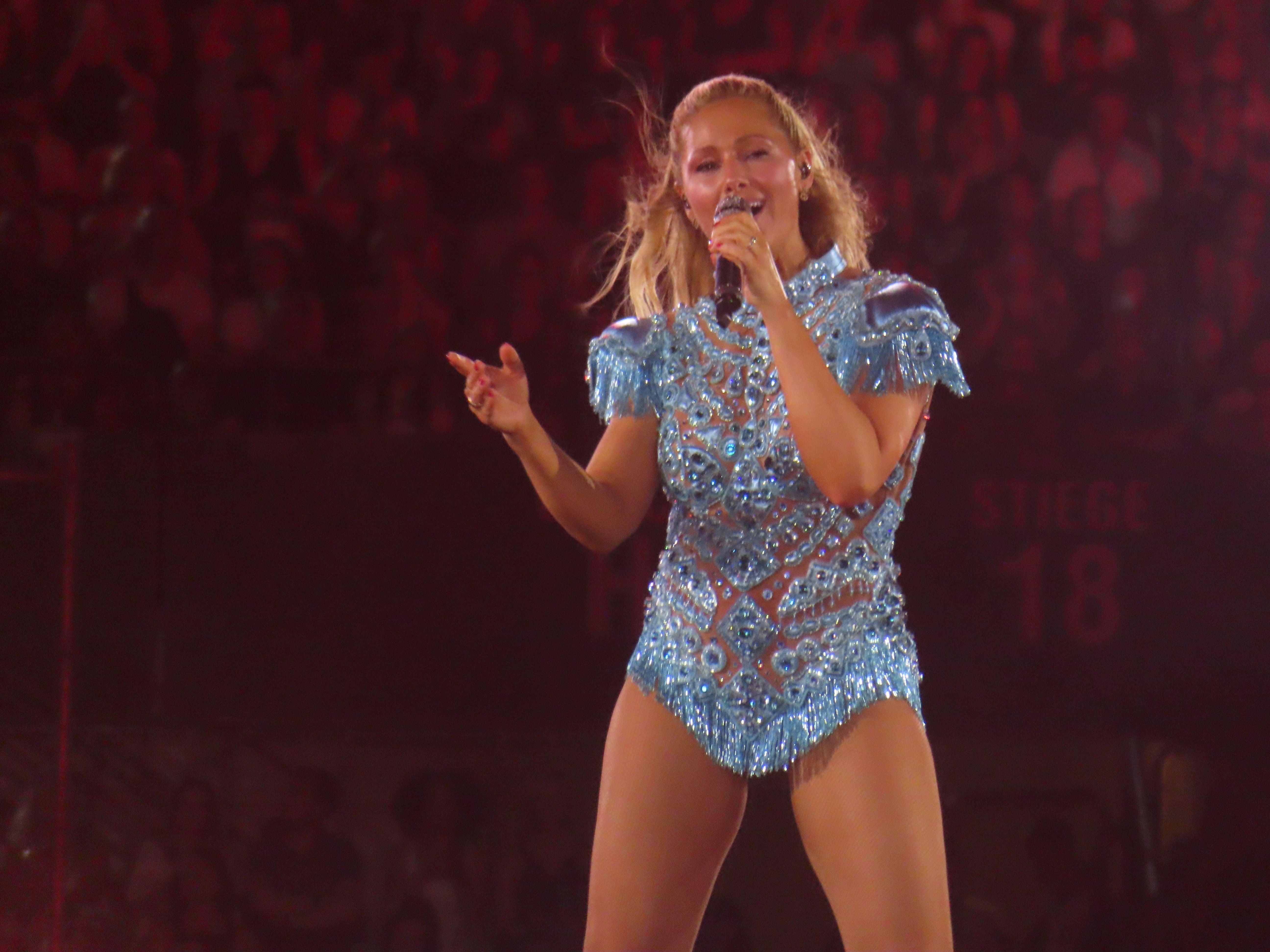 Sängerin Helene Fischer in glitzerndem blauen Kostüm singt auf einer Bühne vor einem Publikum.