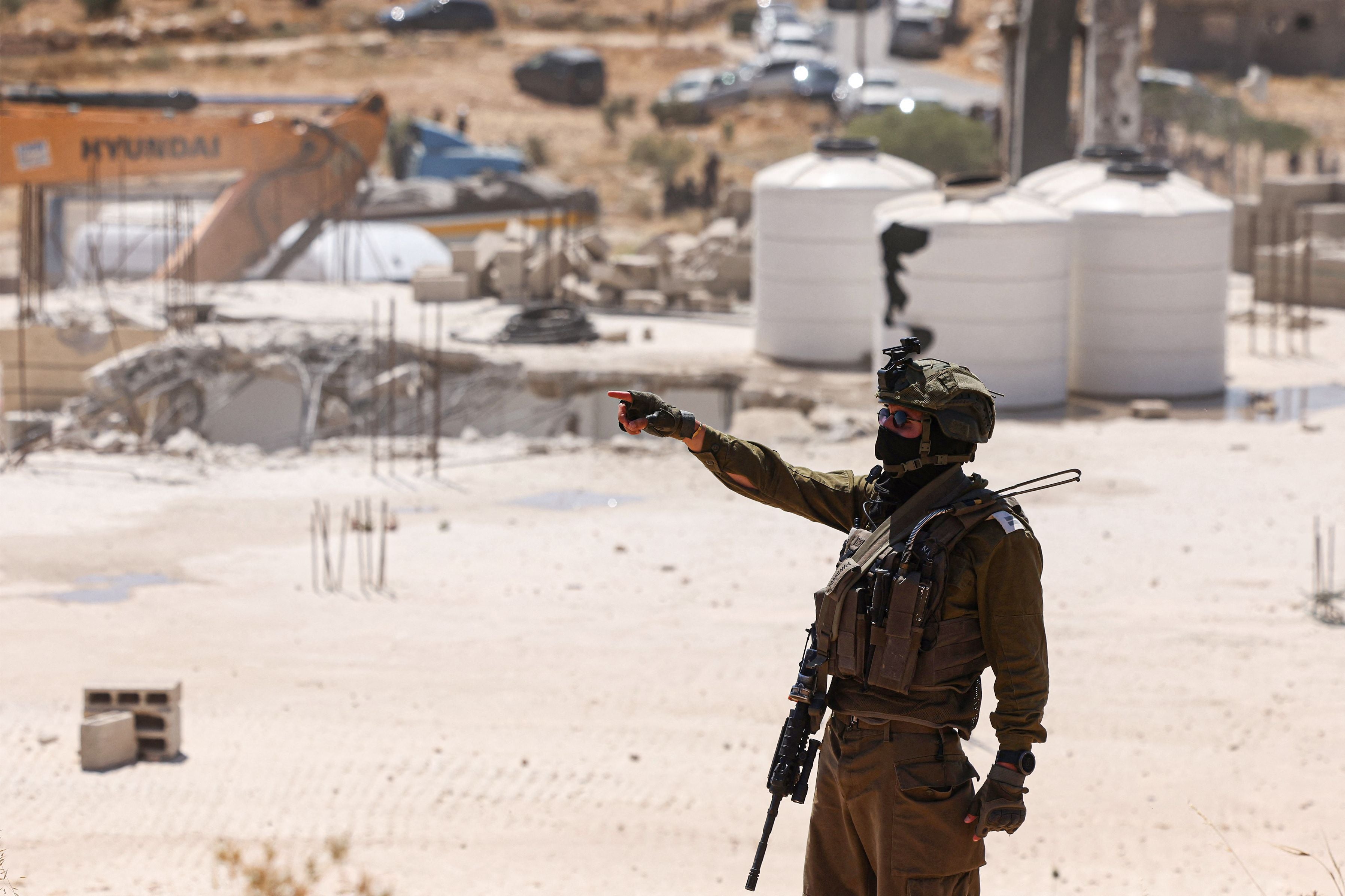 Ein israelischer Soldat steht vor zerstörtem Gebäude und zeigt mit dem Finger in Ar-Rifaiyya, Westjordanland.