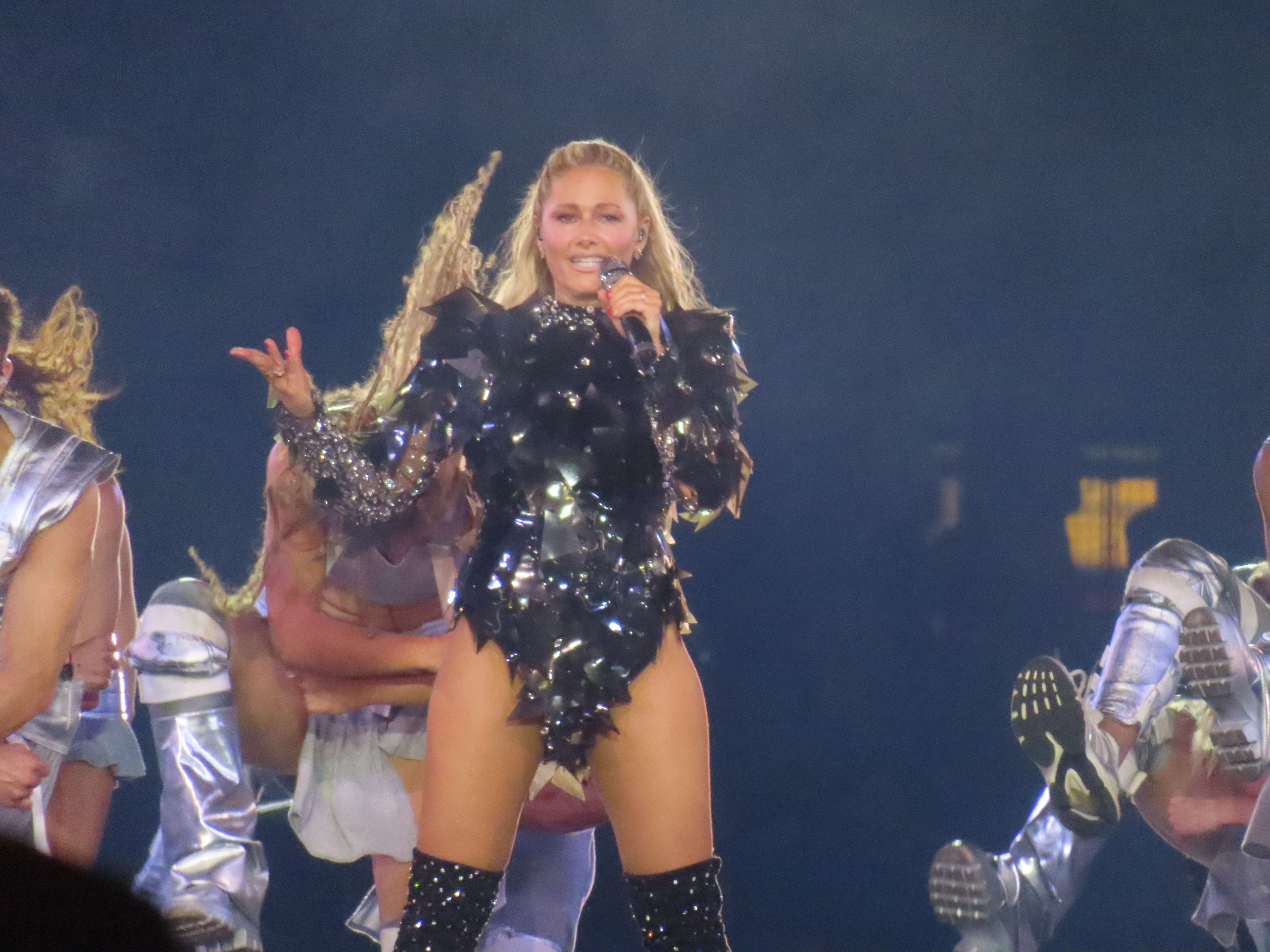 Helene Fischer tritt in einem glitzernden Bühnenoutfit mit Tänzern im Hintergrund auf.
