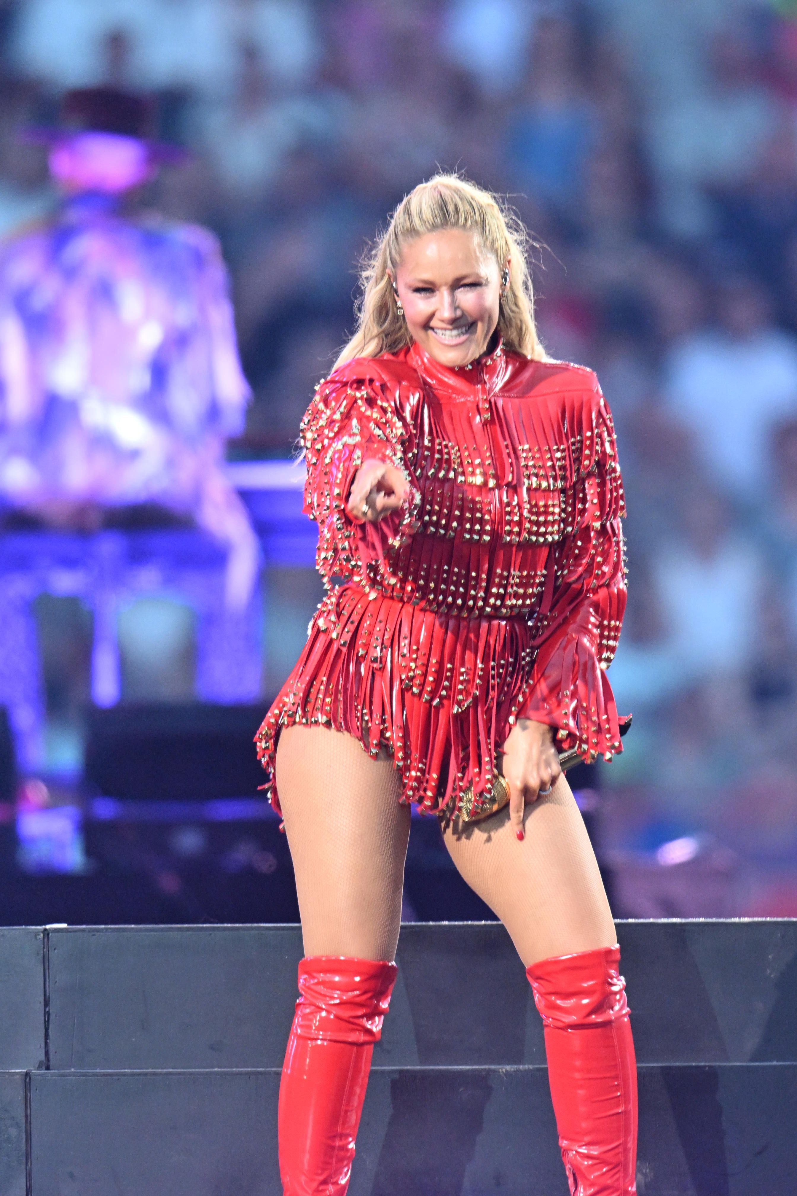 Frau in rotem Bühnenoutfit lächelt und zeigt auf das Publikum bei einem Helene Fischer Konzert.