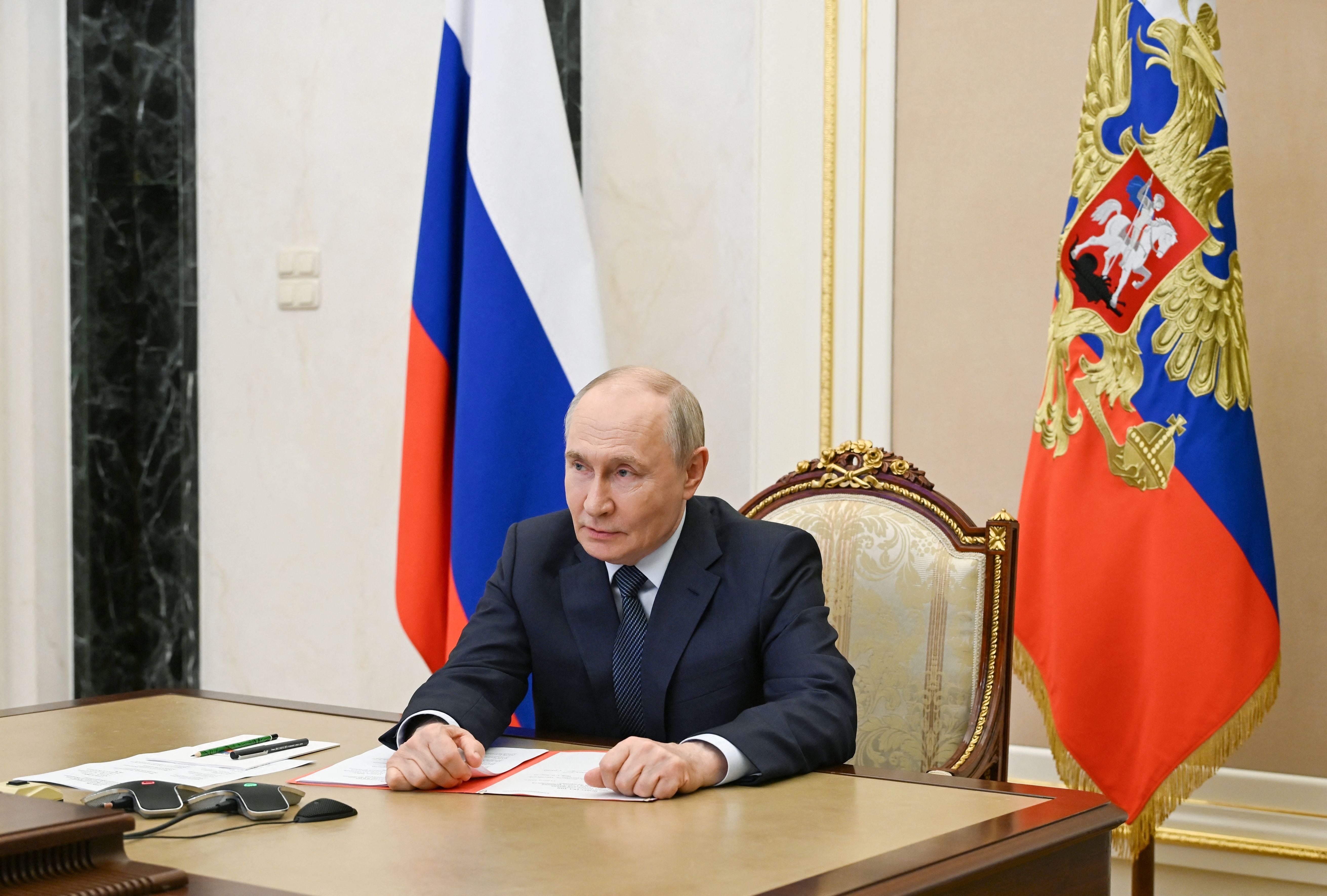 Russlands Präsident sitzt am Schreibtisch vor Flaggen und leitet eine Videokonferenz.