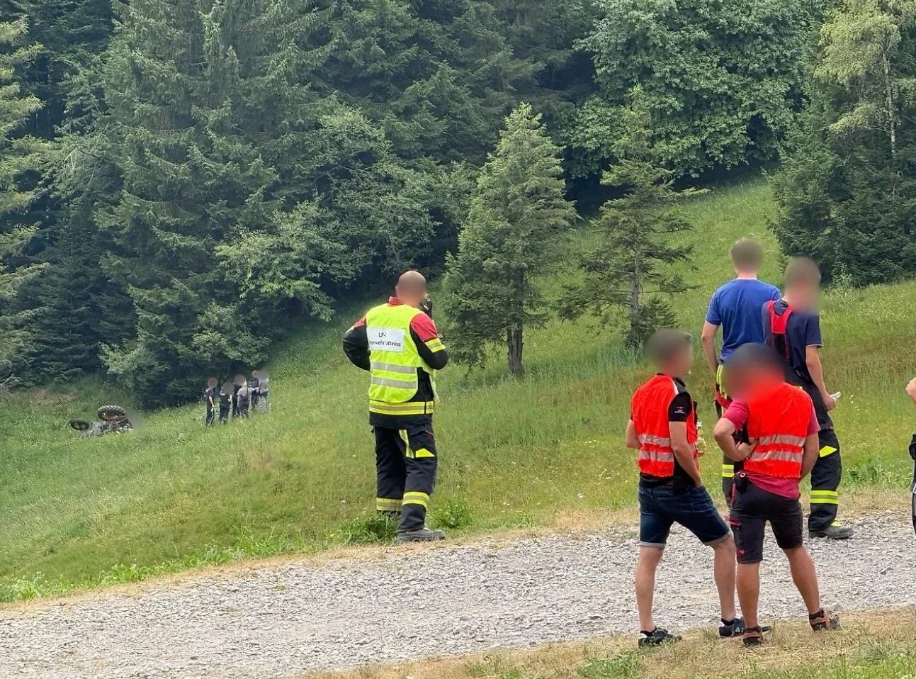 Rettungskräfte stehen auf einer Wiese; im Hintergrund liegt ein umgestürzter Traktor.