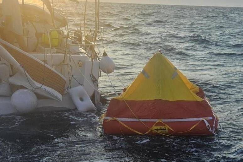 Ein Rettungsfloß treibt neben einem beschädigten Segelboot auf dem Meer.