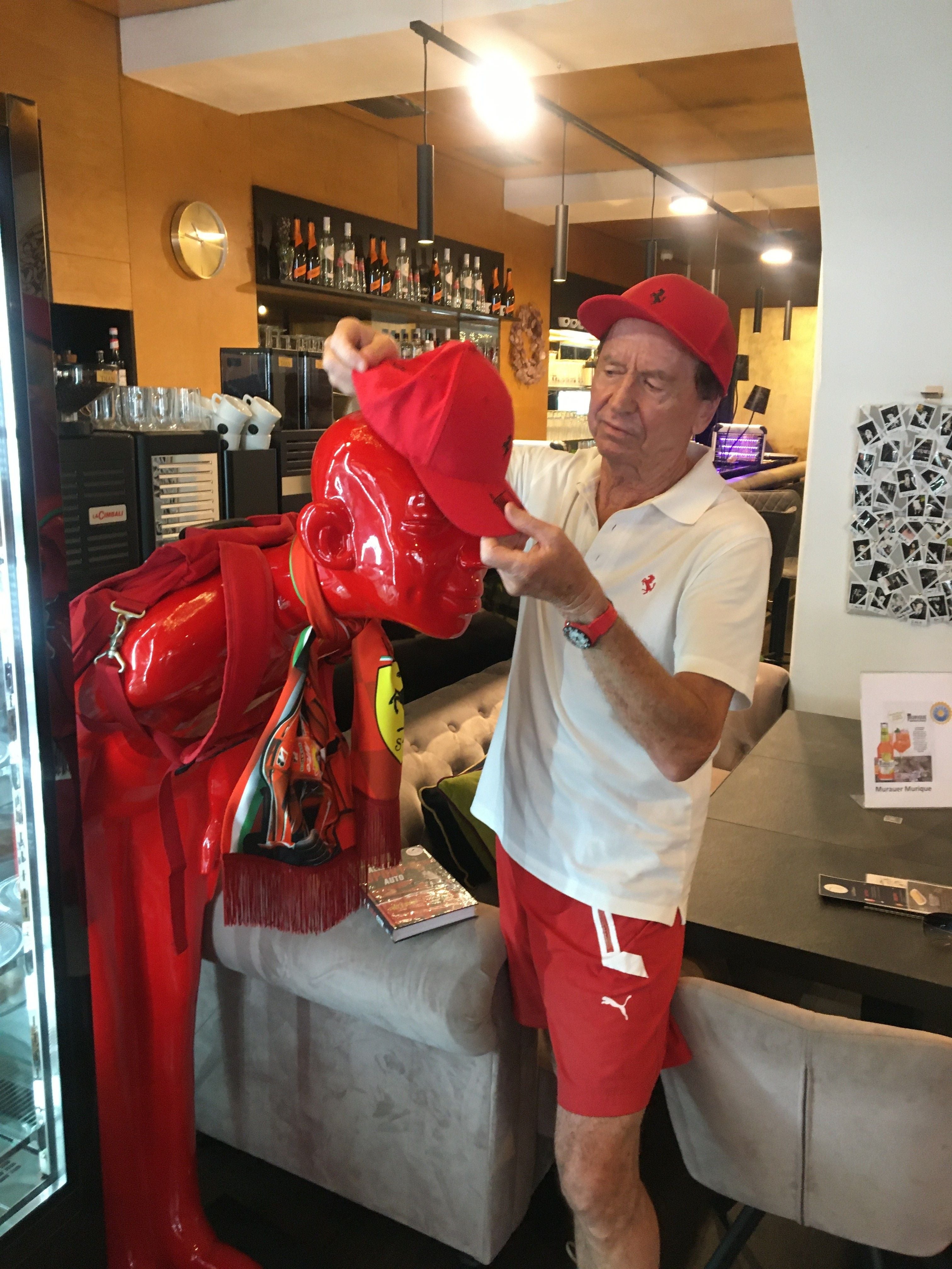 Ein Mann setzt einer roten Skulptur in einem modernen Café eine rote Kappe auf.
