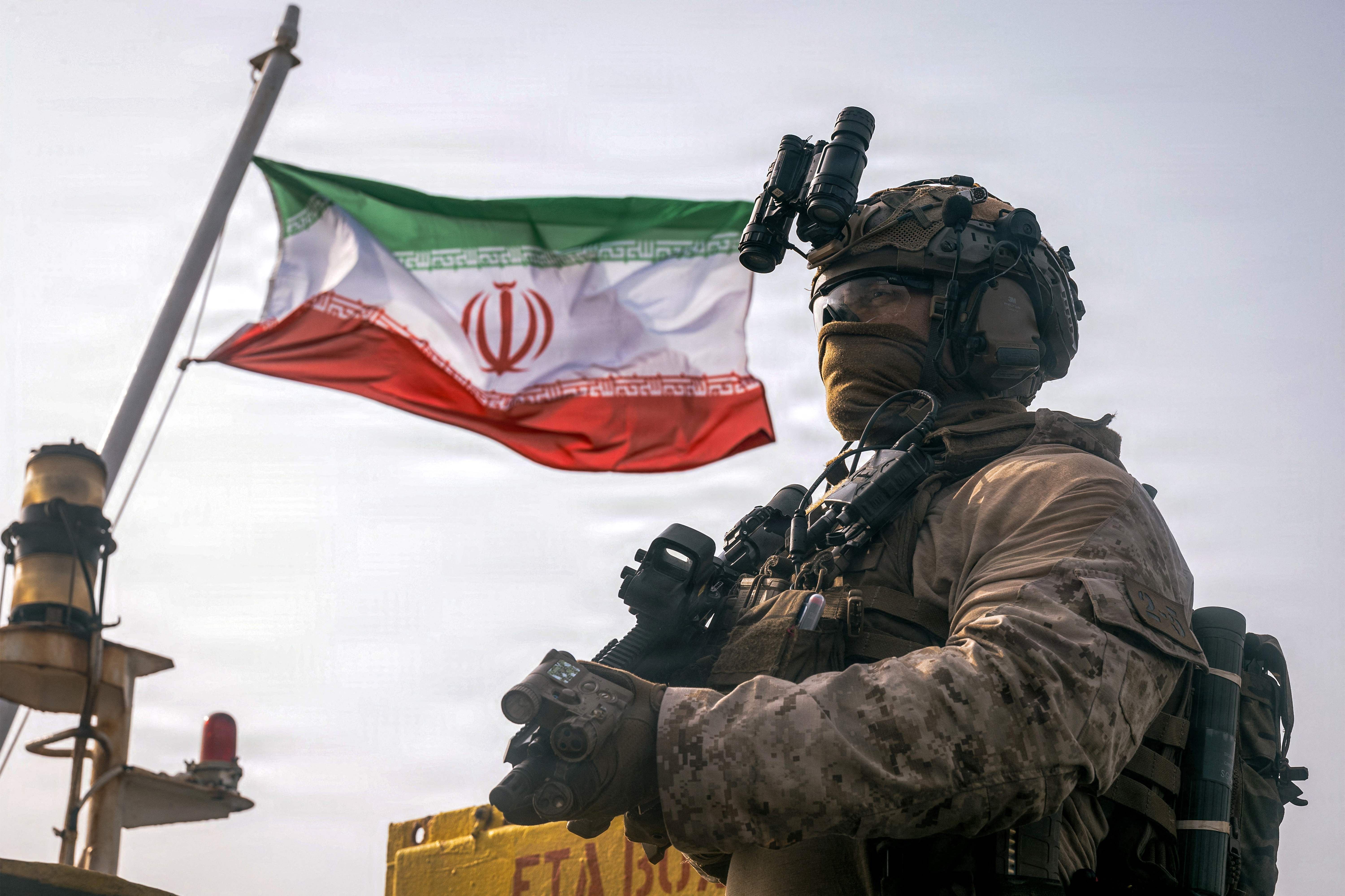 Ein US-Soldat steht bewaffnet vor einer wehenden iranischen Flagge auf einem Schiff.