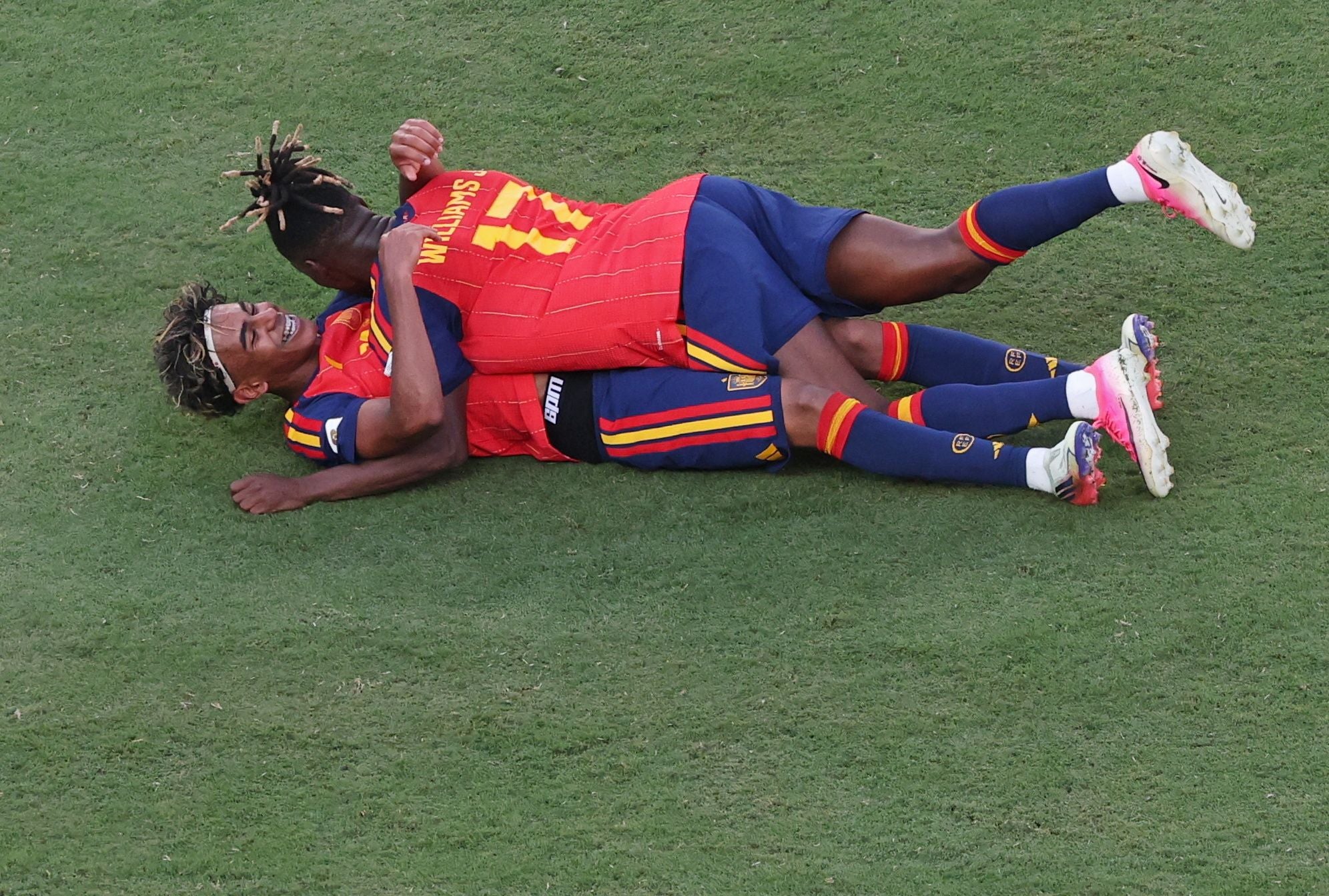 Zwei spanische Fußballspieler feiern jubelnd auf dem Rasen liegend einen Sieg.