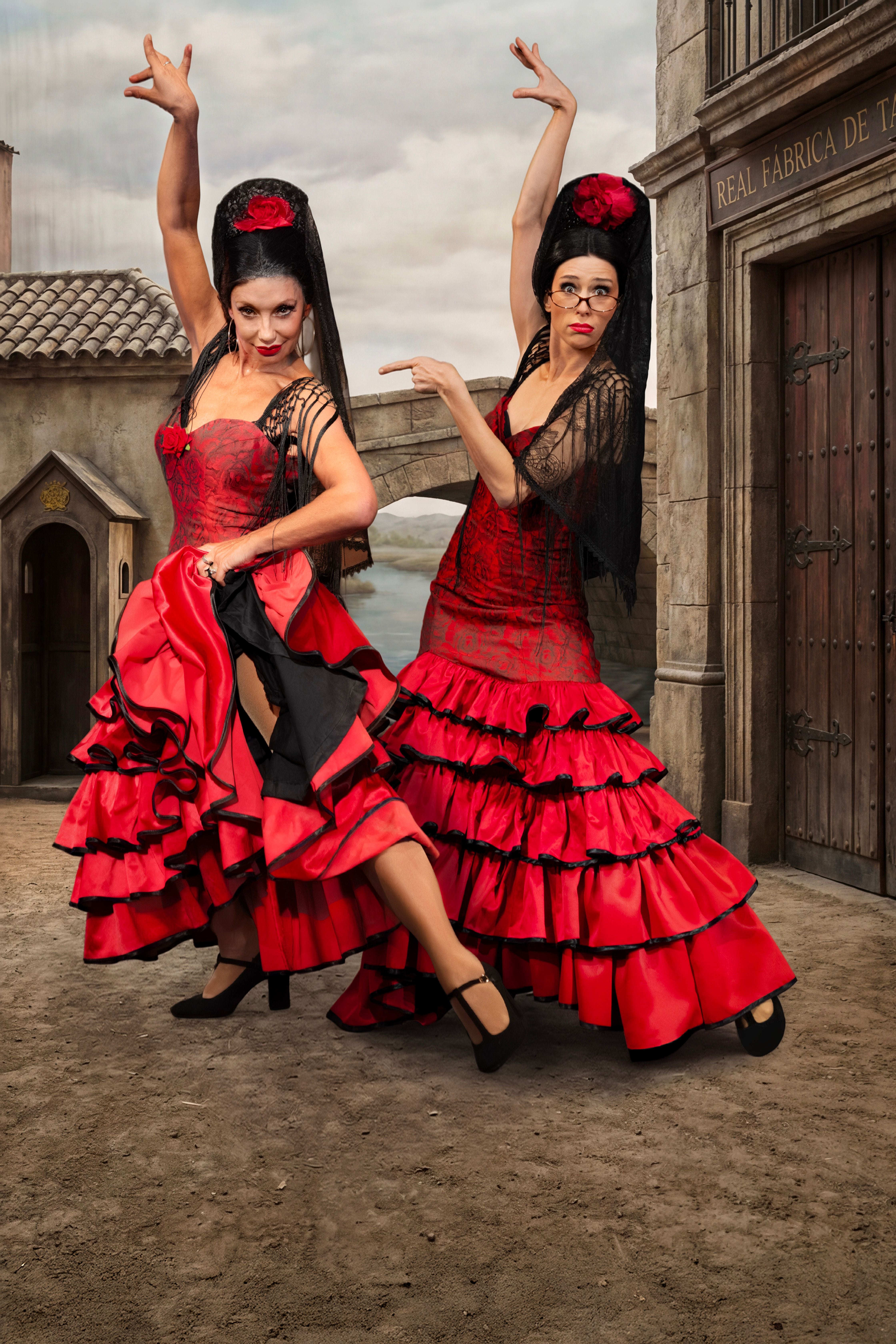 Zwei Frauen tanzen Flamenco in roten Kleidern vor einer historischen Kulisse.