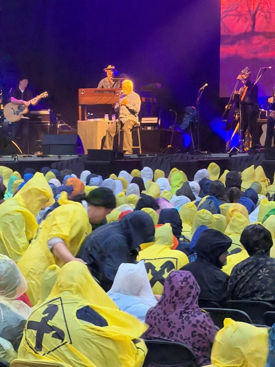 Tom Jones singt auf einer Bühne, das Publikum trägt bunte Regenponchos in Linz.
