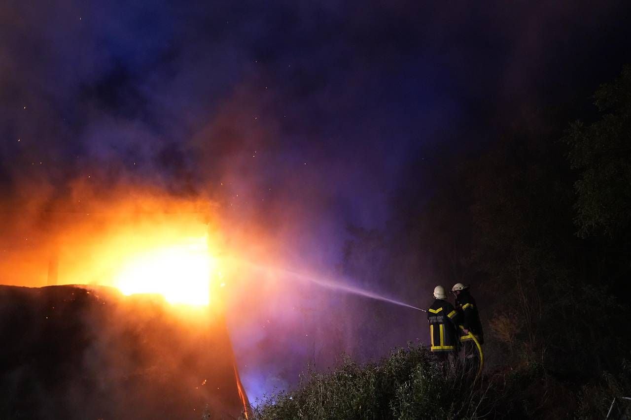 Feuerwehr löscht in der Nacht einen Großbrand in einem Strohlager mit Wasserschlauch.