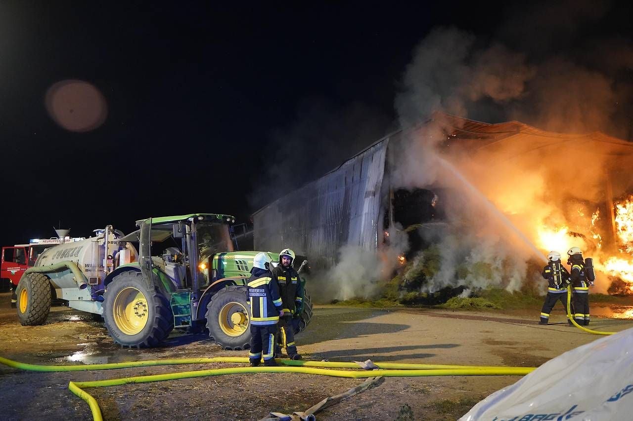 Feuerwehr löscht Brand in einem Strohlager bei Nacht, starke Rauchentwicklung und Flammen.