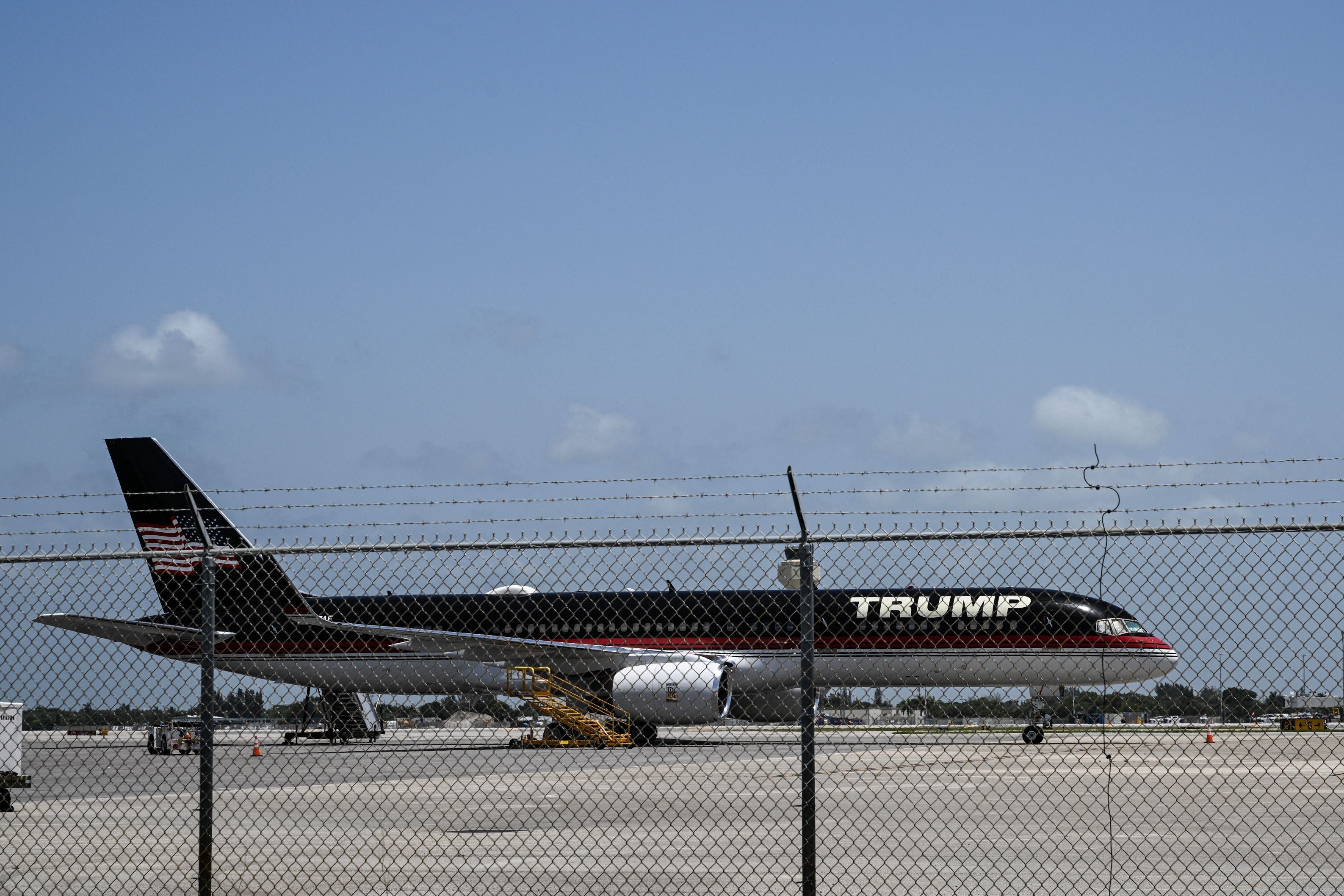 Ein Flugzeug mit der Aufschrift "TRUMP" steht hinter einem Zaun auf einem Flughafen.