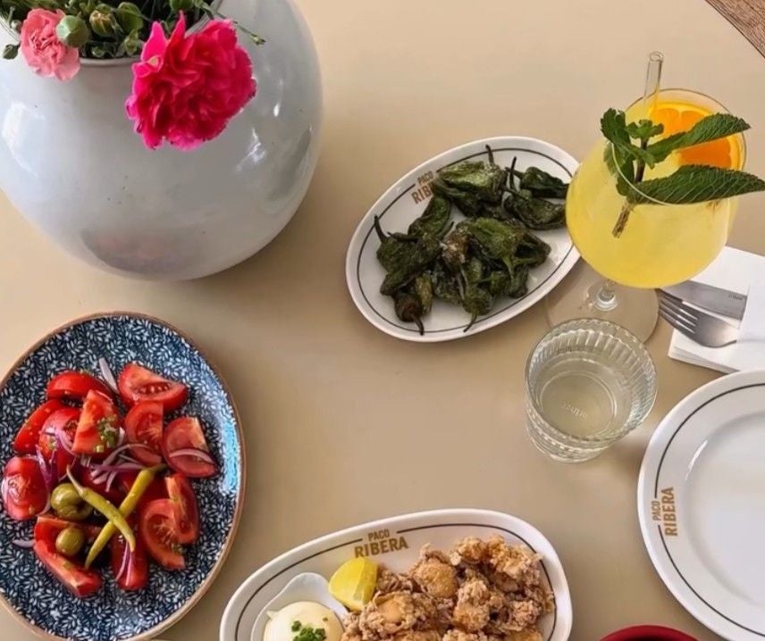 Tisch mit Tapas, Getränk, Wasserglas, Blumen und Tellern im Restaurant Paco Ribera.