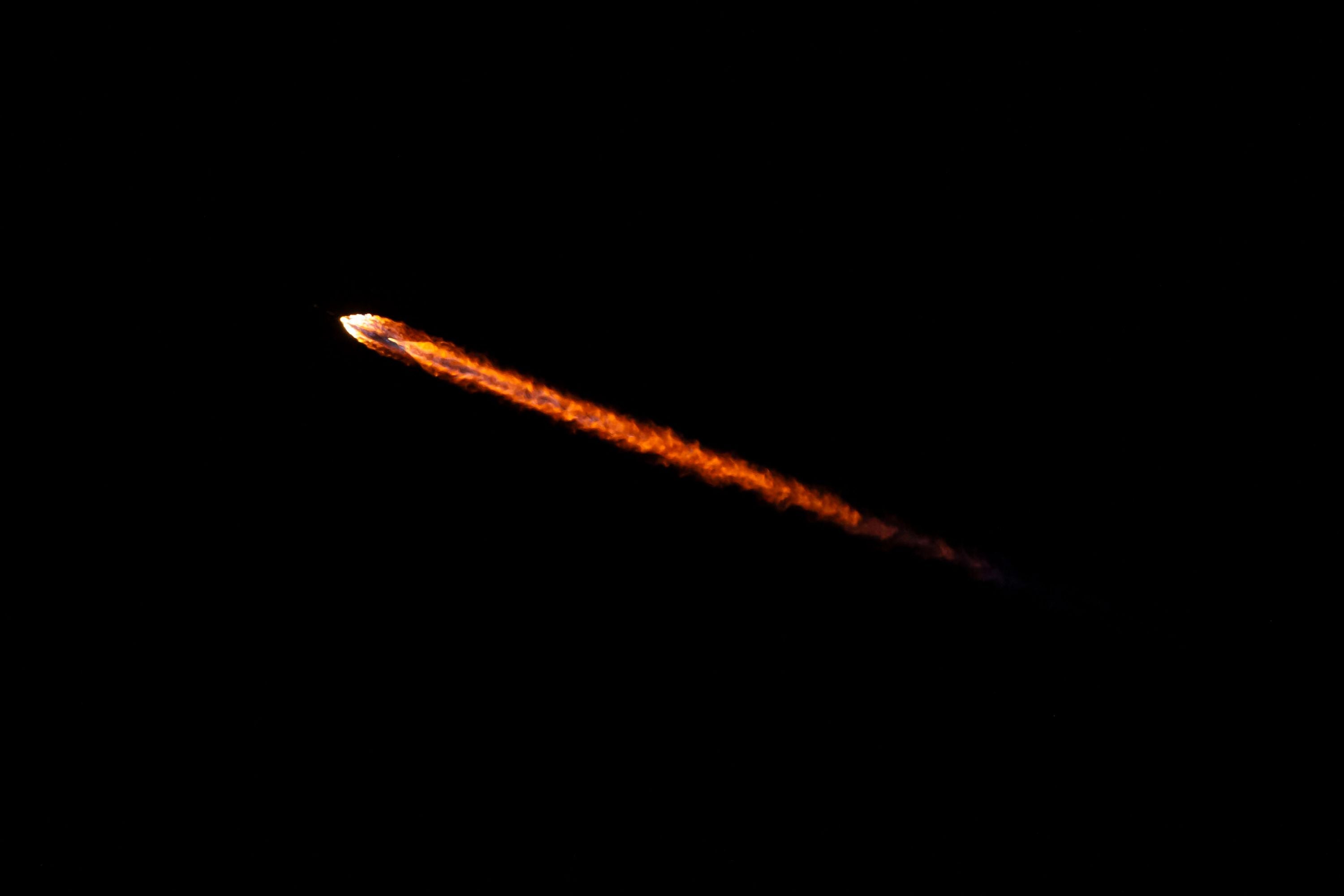 Eine Falcon-9-Rakete mit leuchtender Spur startet in dunkler Nacht.
