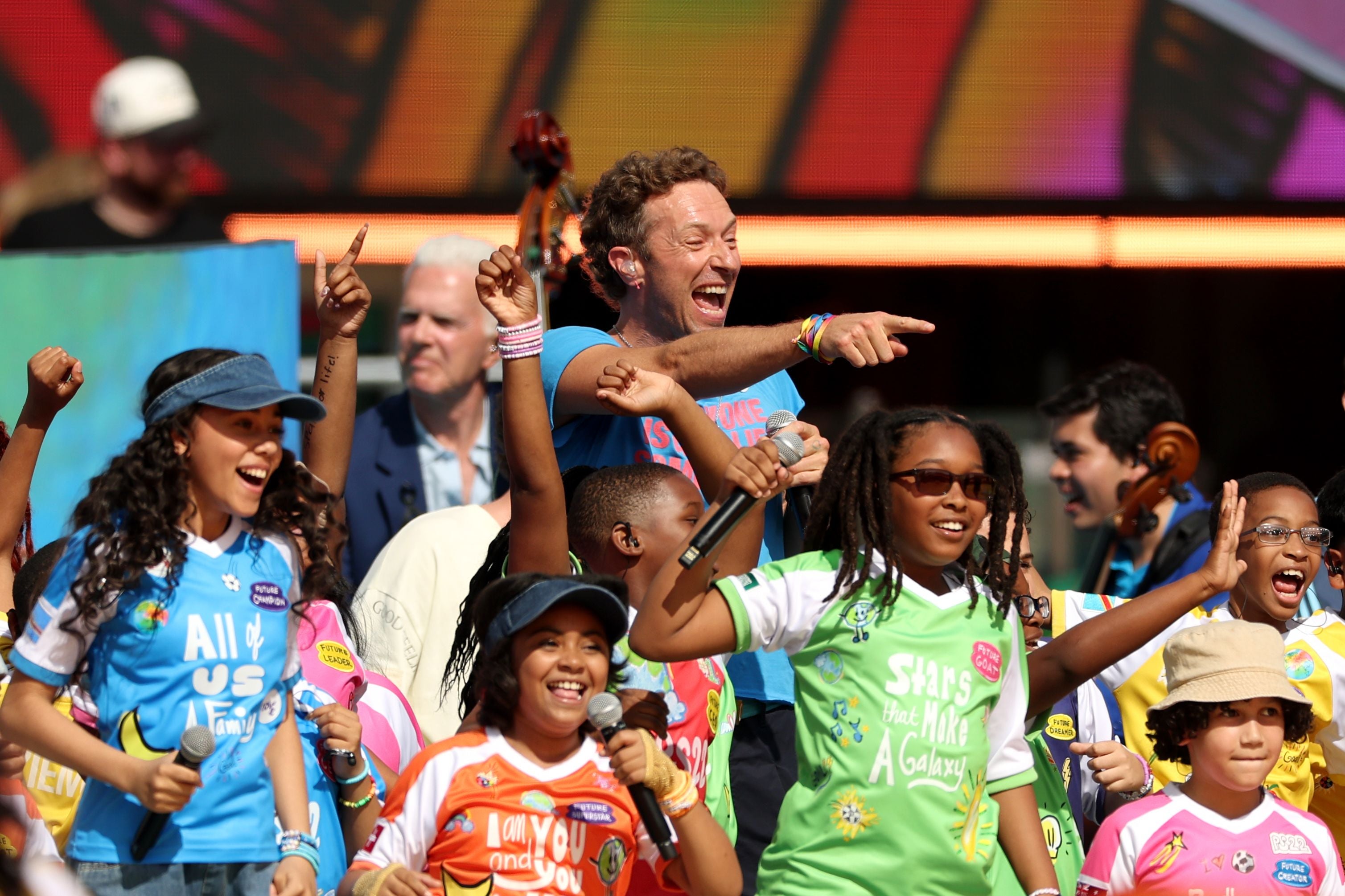 Chris Martin singt begeistert mit fröhlichen Kindern auf einer bunten Bühne beim FIFA WM-Finale 2026.