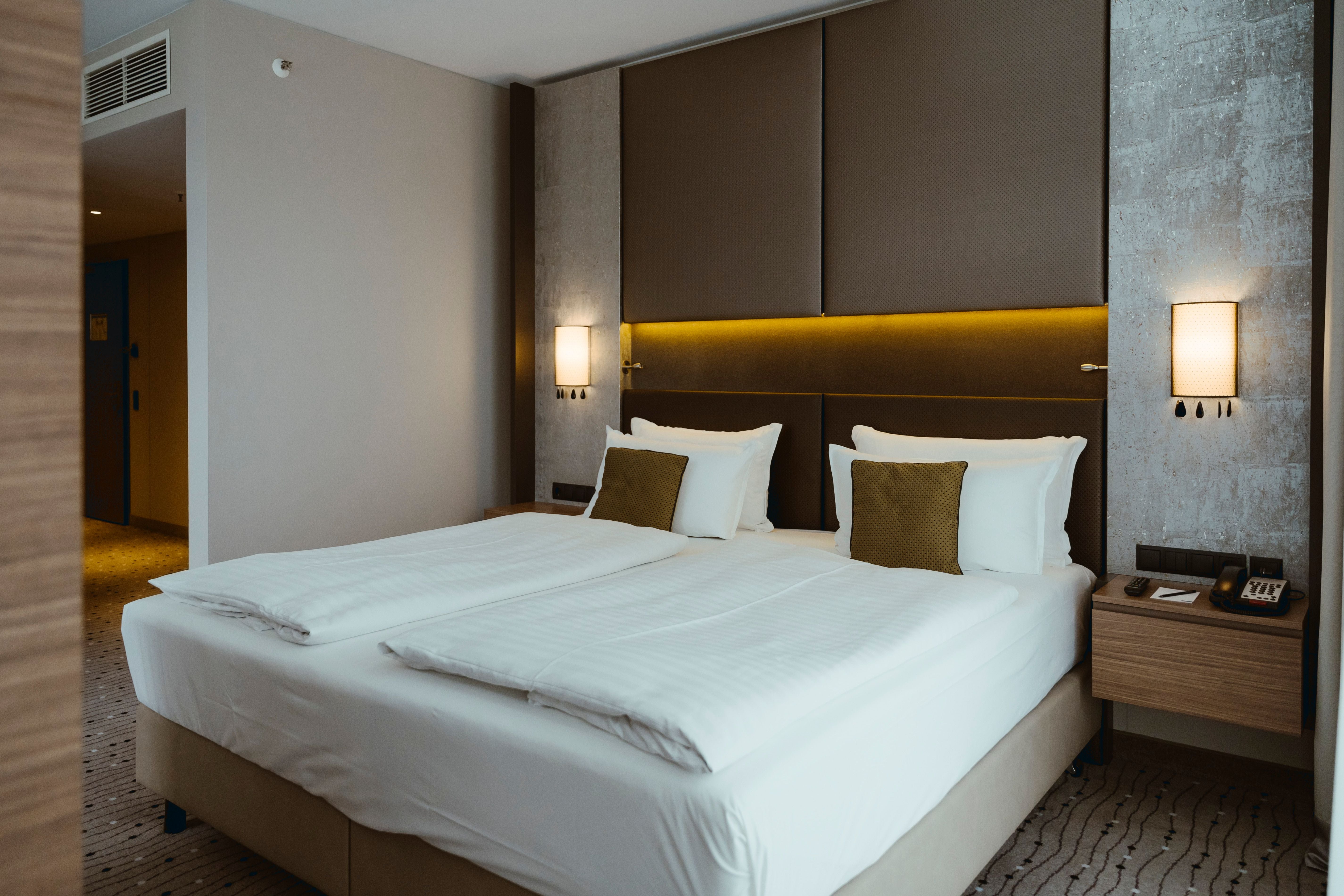 Modernes Hotelzimmer mit großem Doppelbett, weißen Bettwaren und braunen Kissen.