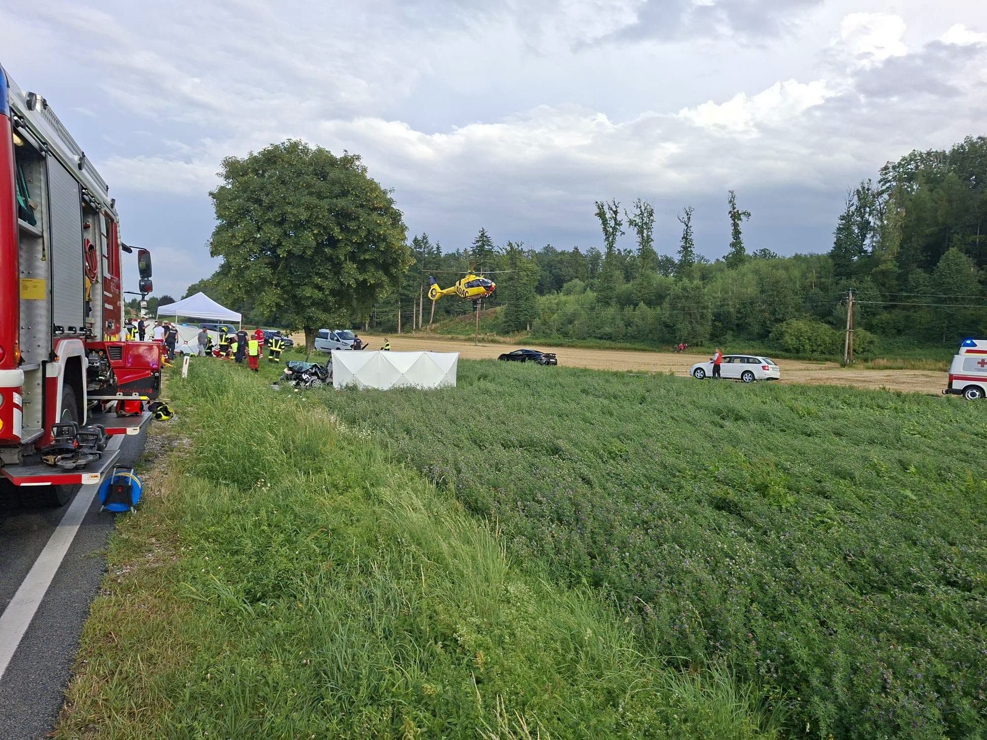 Unfallstelle mit Feuerwehr, Rettungshubschrauber, Rettungswagen und Einsatzkräften auf einem Feld.