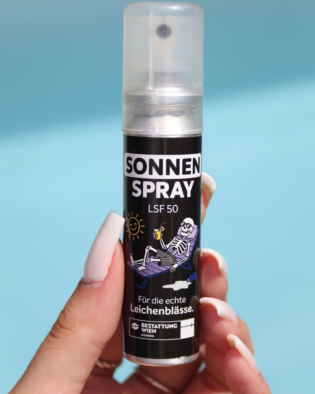 Eine Hand hält eine Sonnencreme-Flasche mit Skelett-Motiv und der Aufschrift „Für echte Leichenblässe“.