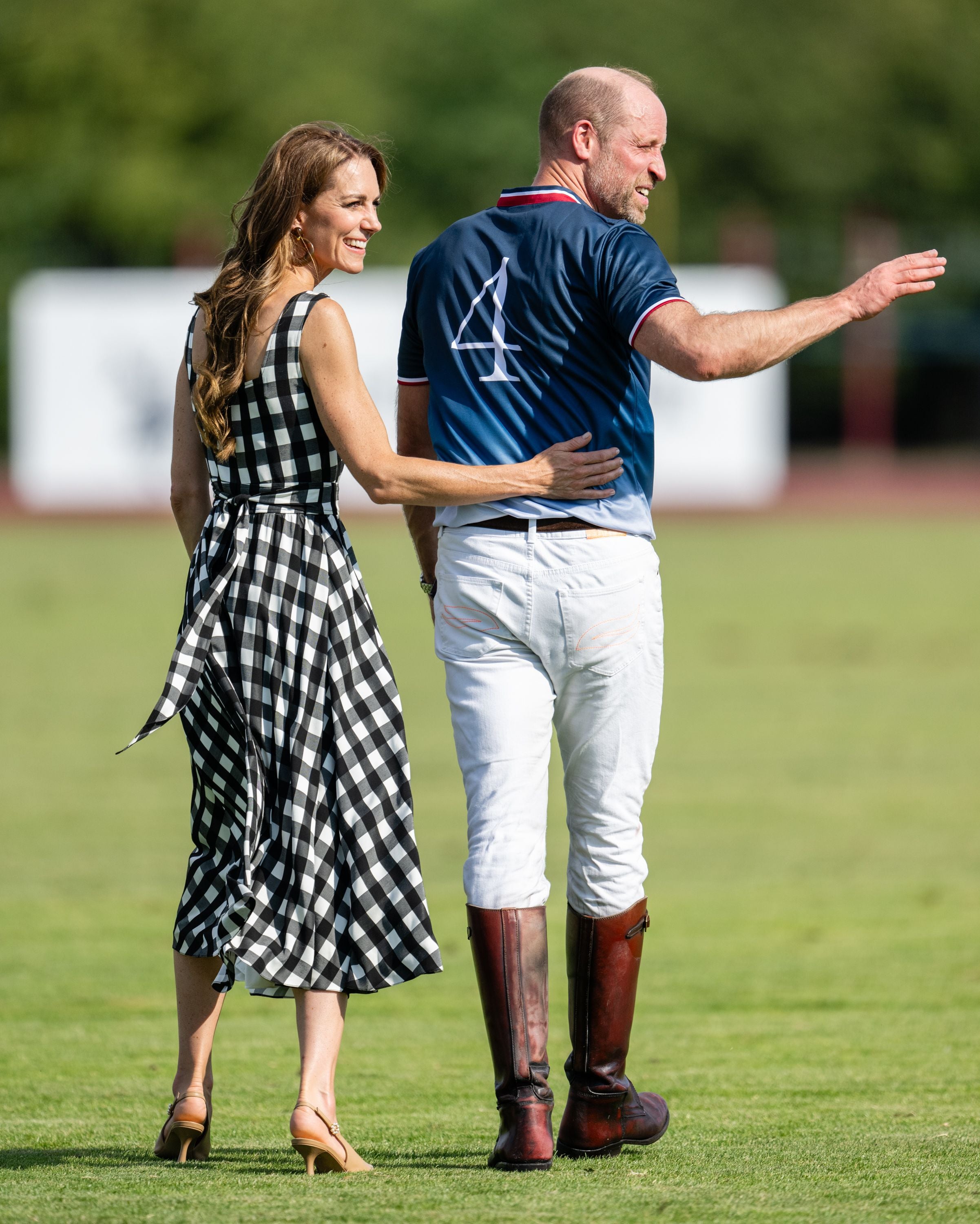 Eine Frau im karierten Kleid und ein Mann in Polokleidung gehen gemeinsam über ein Spielfeld.