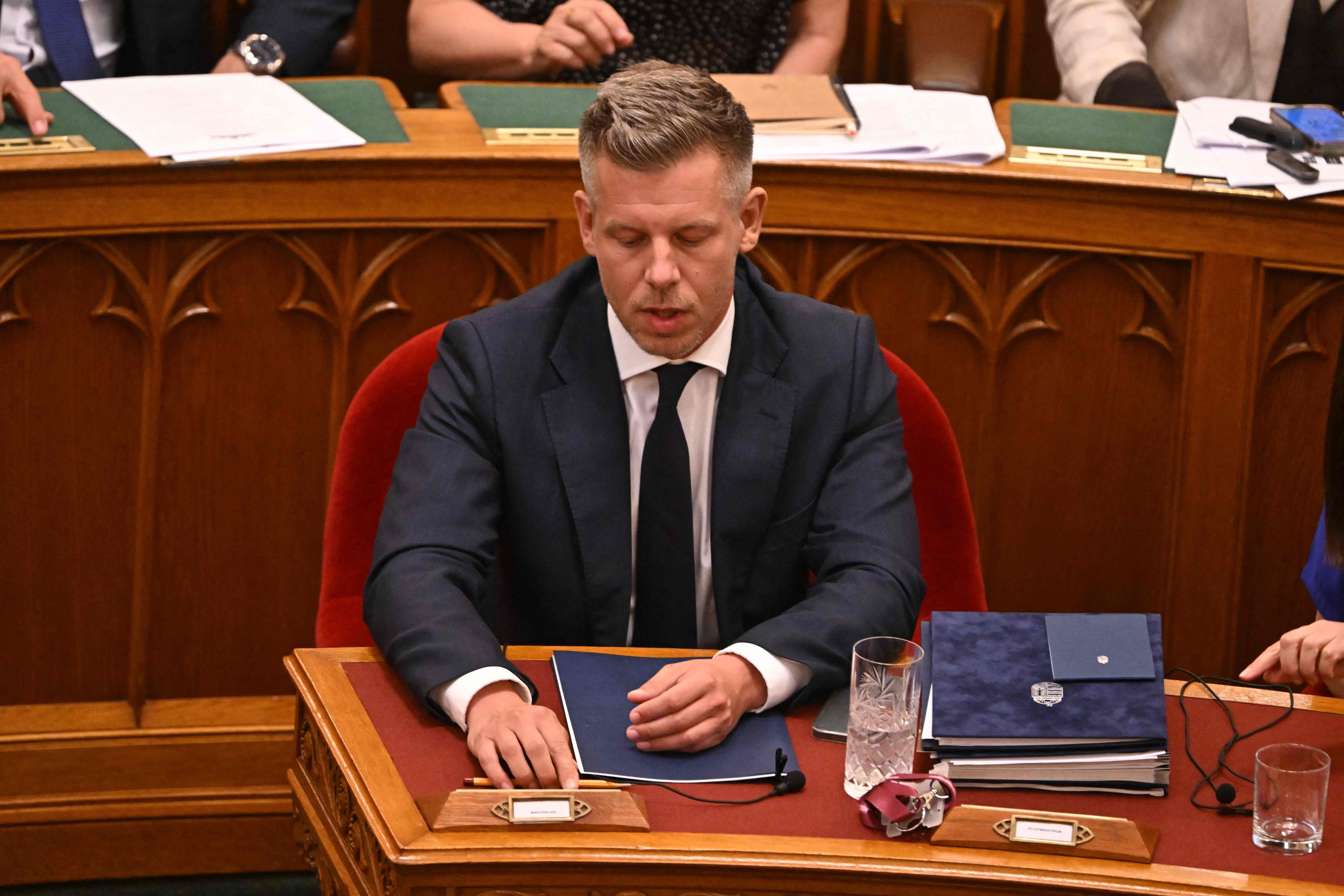 Ein Mann im Anzug sitzt an einem Schreibtisch im Parlament mit Akten und einem Glas Wasser.