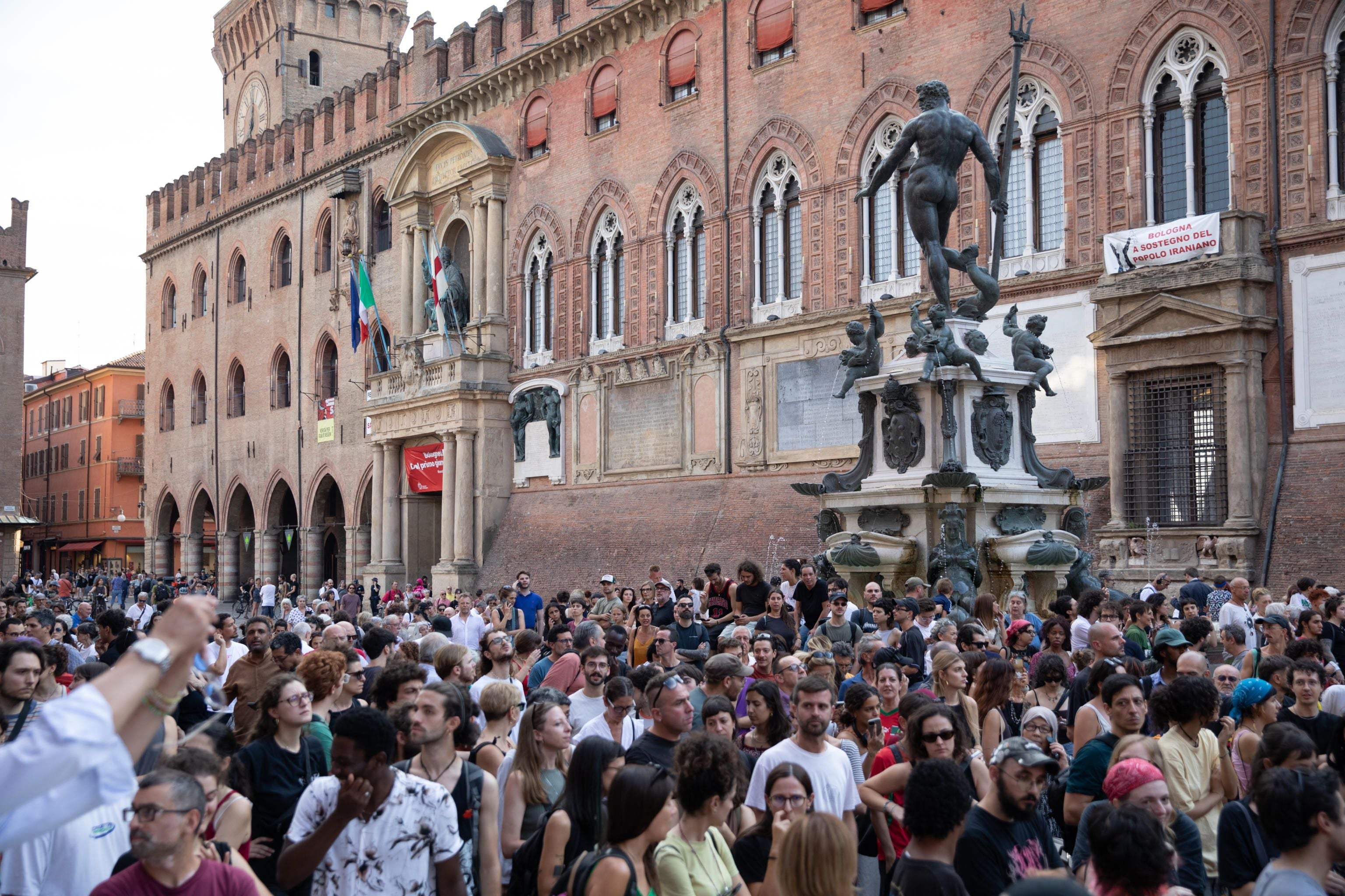 Menschenmenge demonstriert vor historischer Fassade und Neptunbrunnen in Bologna, Italien.