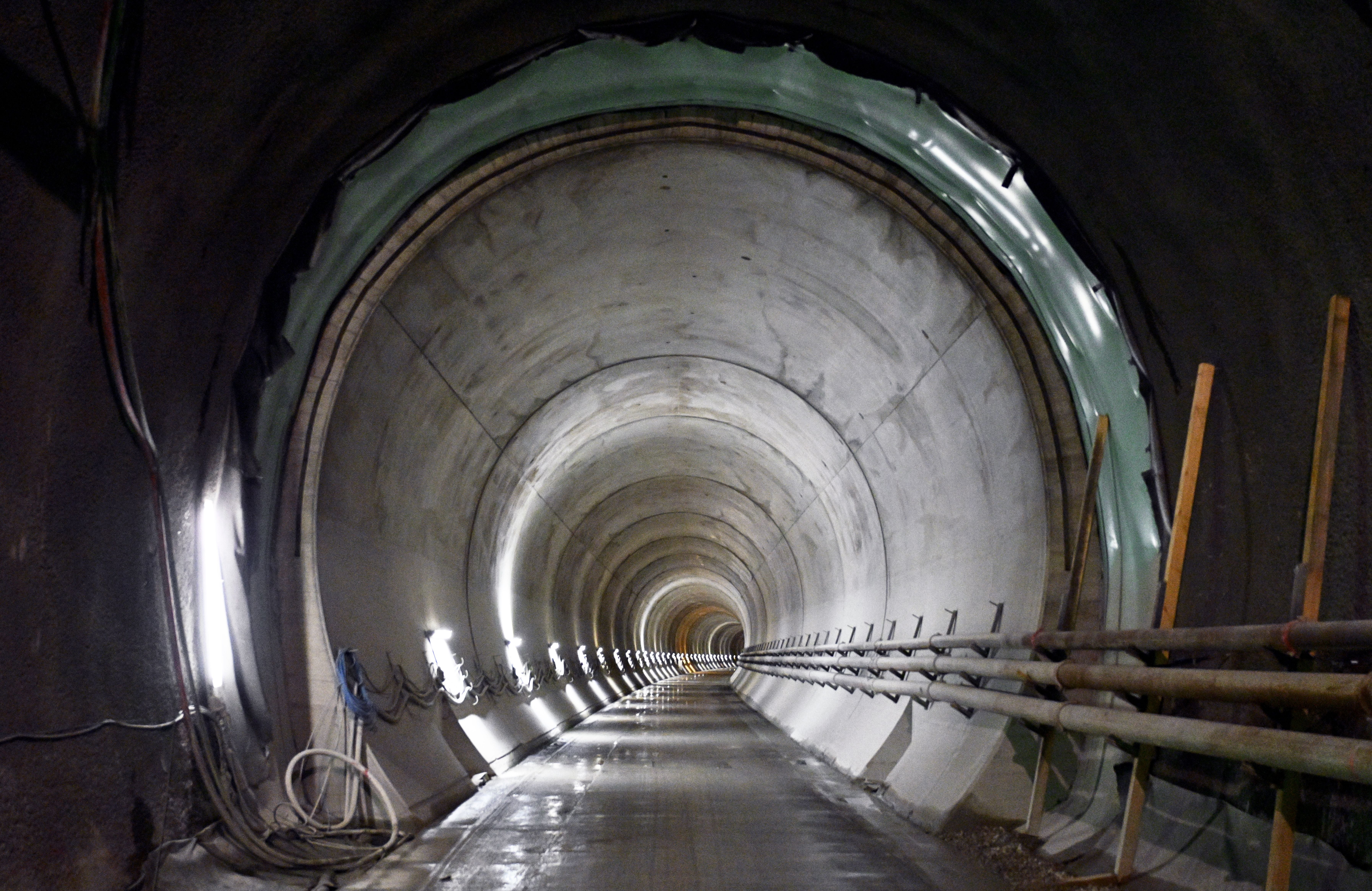 Blick in eine beleuchtete Tunnelröhre des Semmering-Basistunnels mit Kabeln und Rohren an den Seiten.