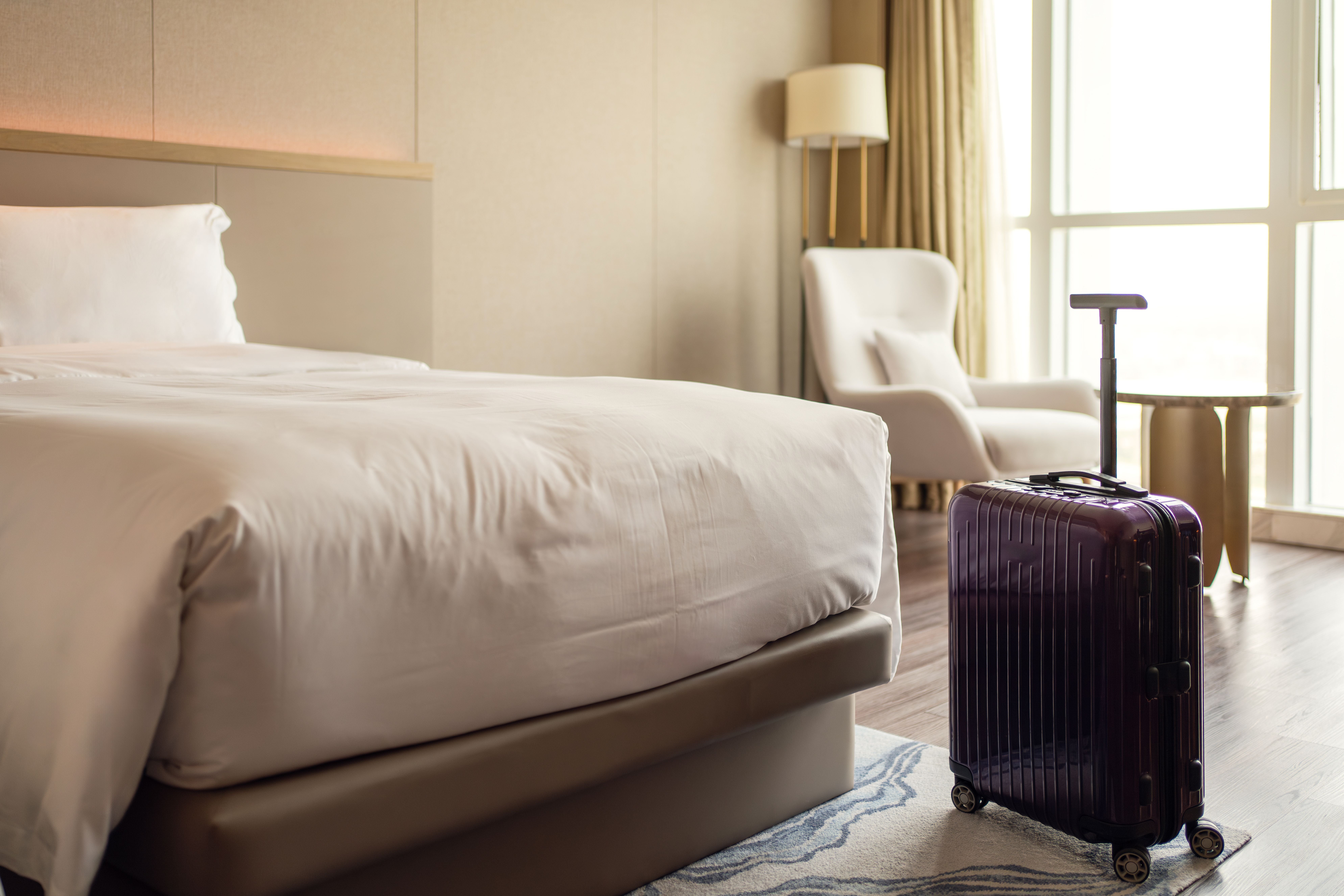 Modernes Hotelzimmer mit gemachtem Bett und violettem Koffer auf dem Teppich.