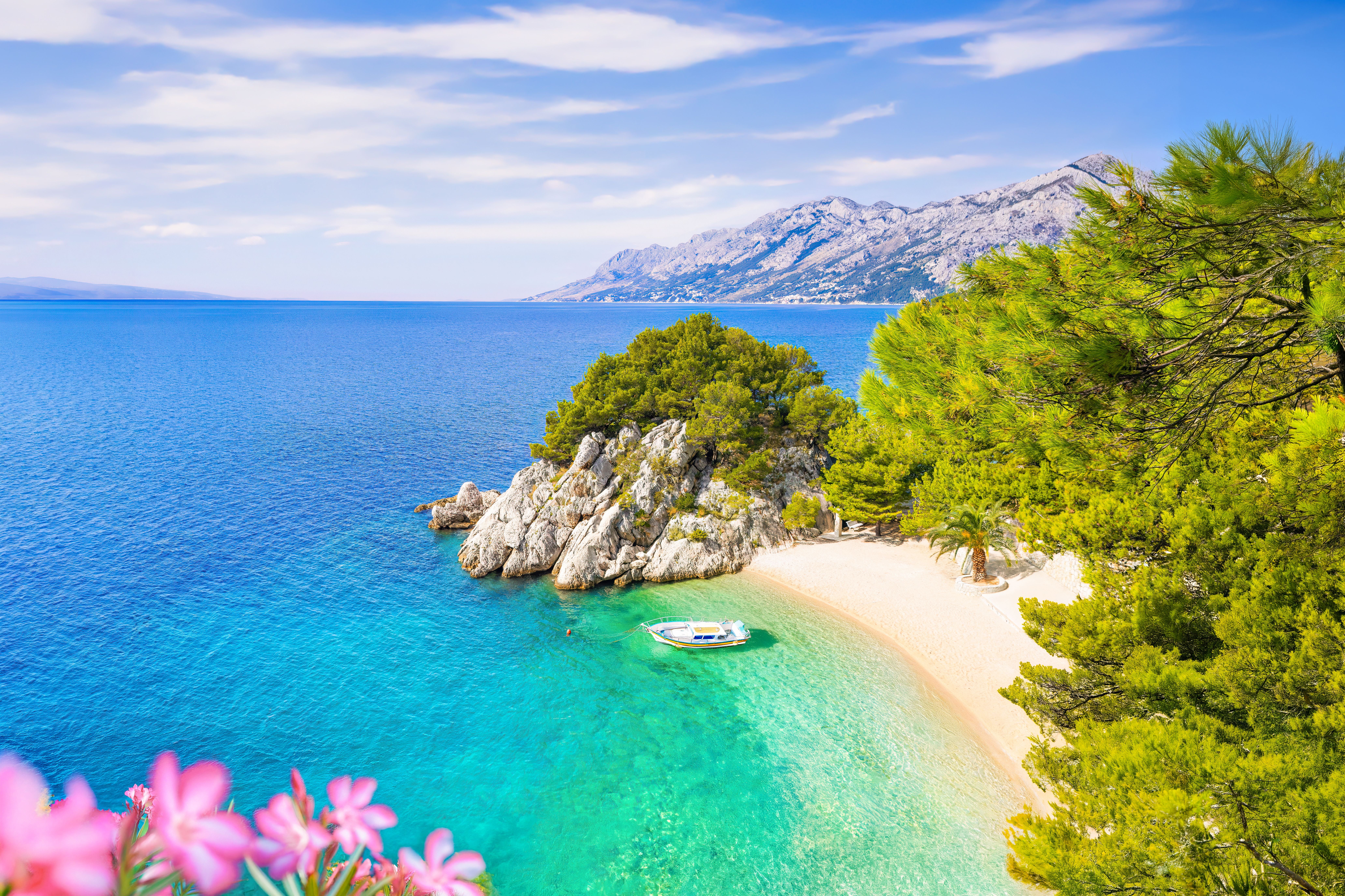 Kristallklares Wasser, Kiesstrand, ikonischer Felsen mit Kiefern und Boot an der Küste von Brela, Kroatien.