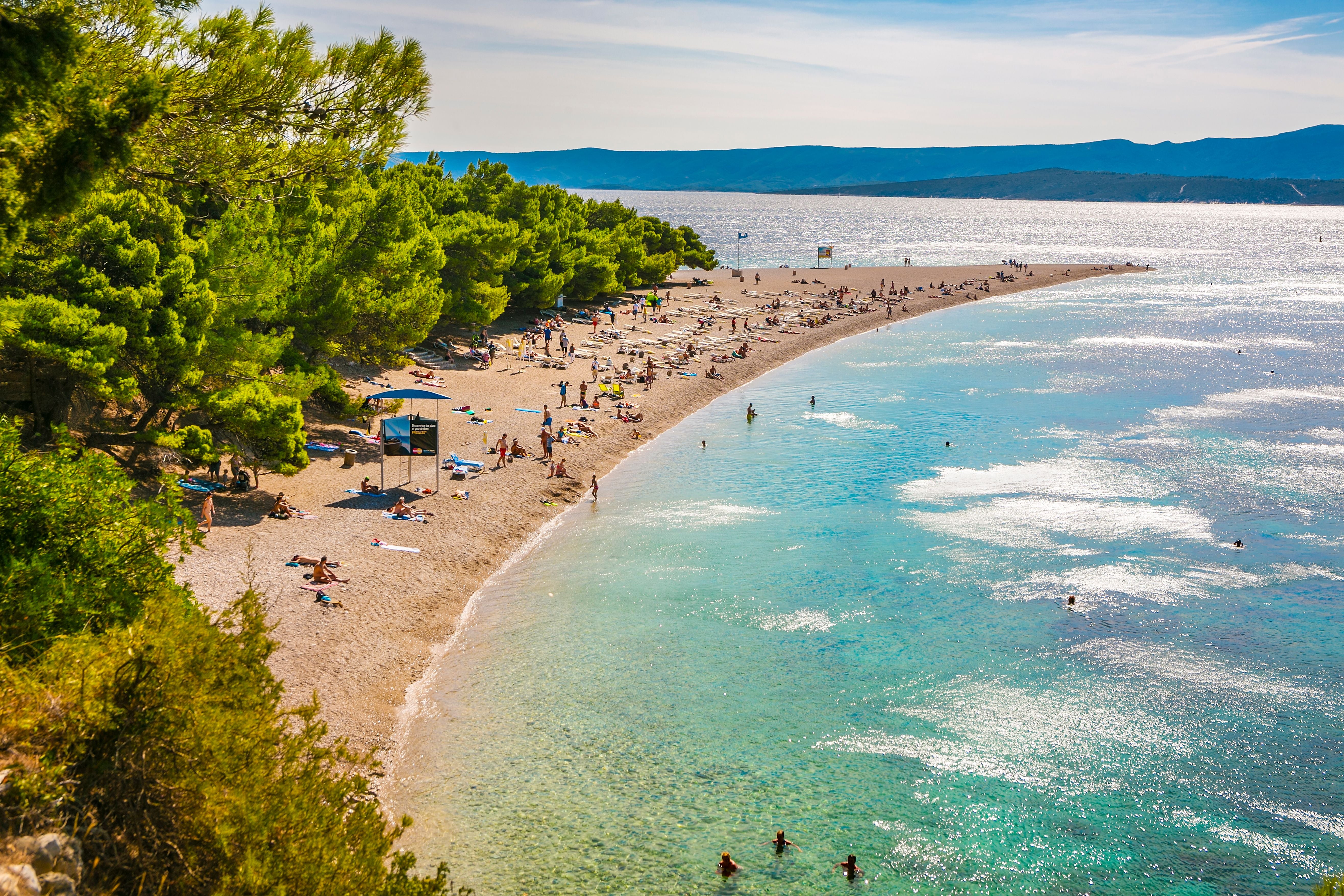 Strand Zlatni Rat mit türkisblauem Wasser, Badegästen und Pinien auf der Insel Brac, Kroatien.