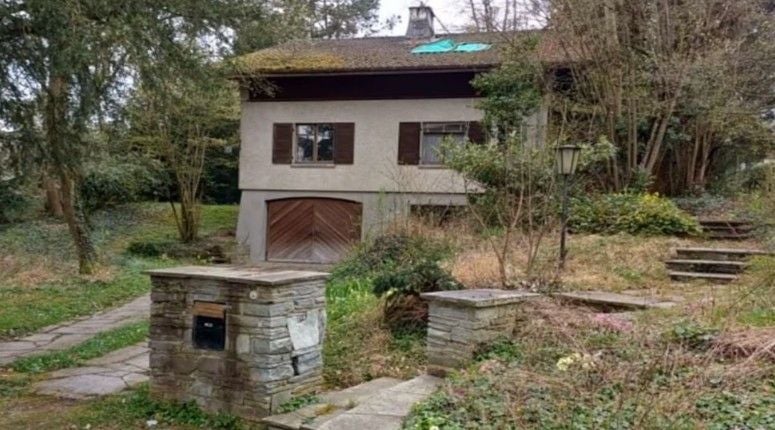 Altes Einfamilienhaus mit Garage, Garten und Natursteinmauer in der Schweiz.