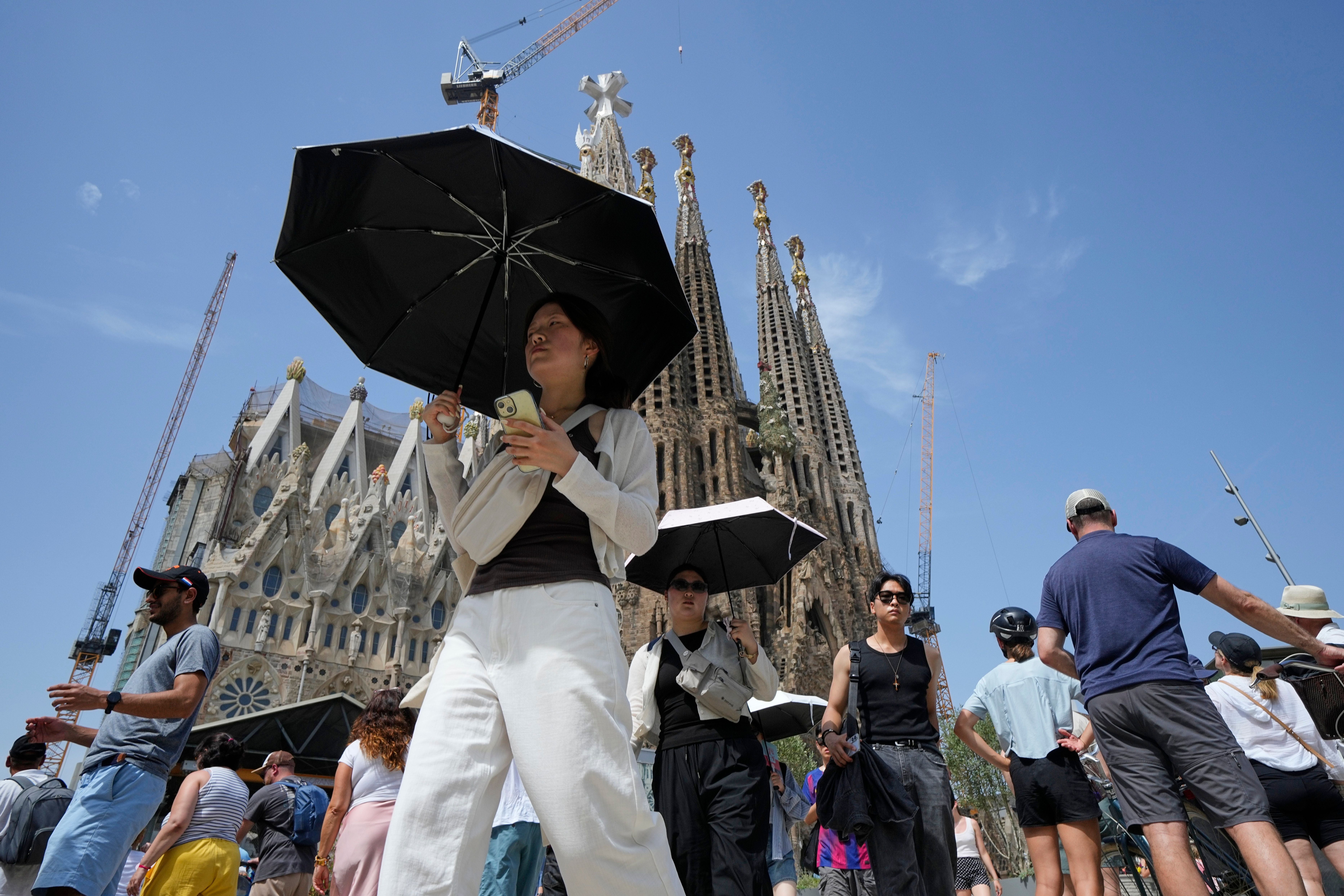 Touristen schützen sich mit Sonnenschirmen vor der Sagrada Familia in Barcelona vor der Hitze.