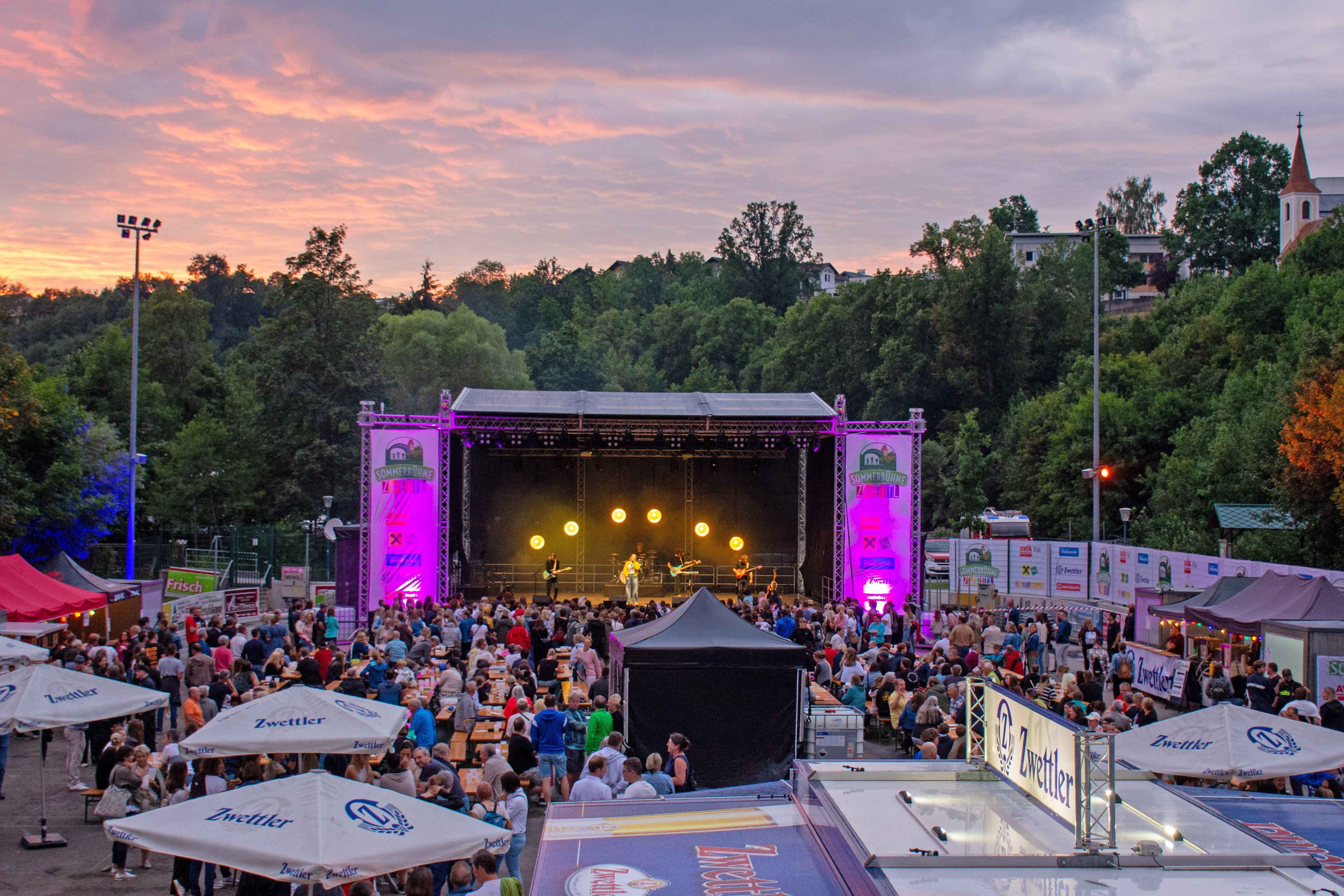 Open-Air-Konzert bei Sonnenuntergang auf der Sommerbühne Zwettl mit Publikum und Bierständen.