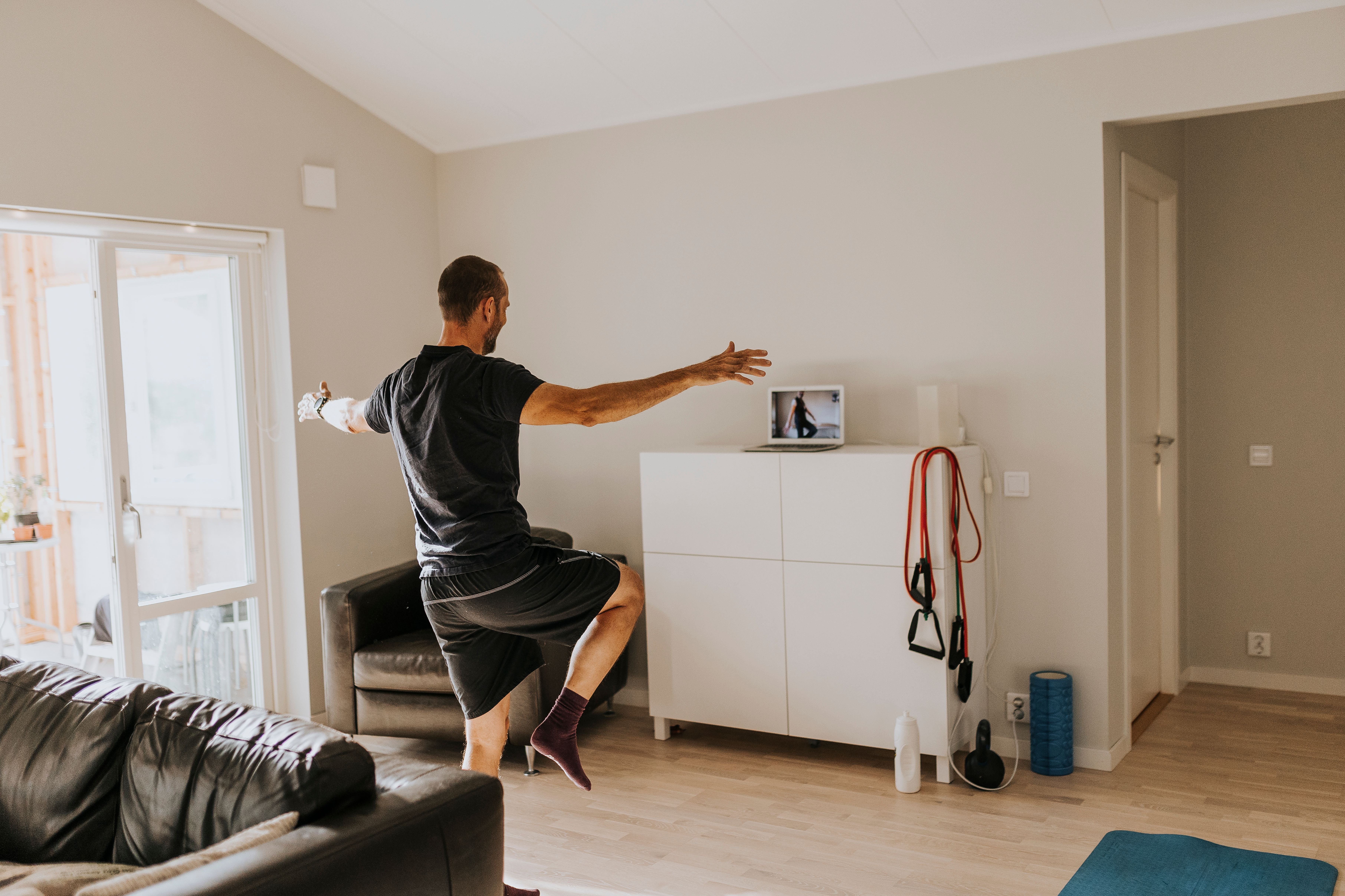 Mann macht Fitnessübungen im Wohnzimmer vor einem Laptop mit Online-Training.