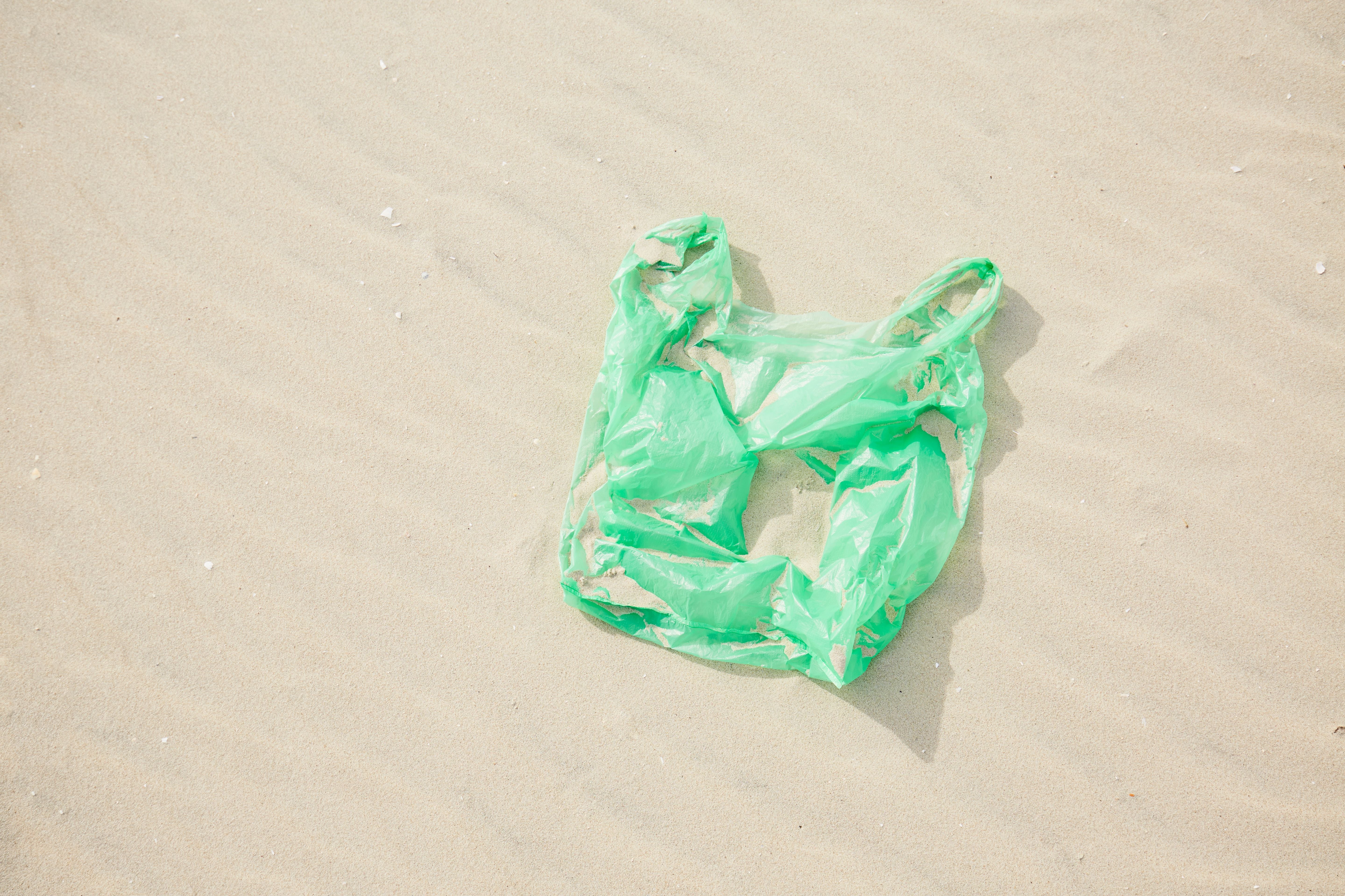 Grüne Plastiktüte liegt im Sand am Strand.