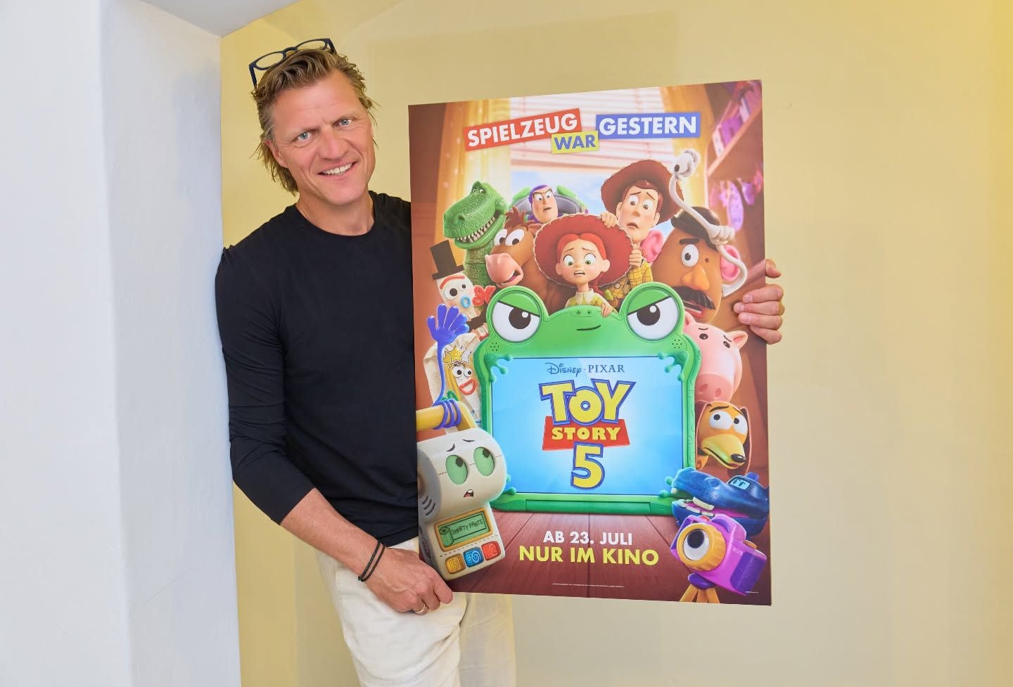 Ein Mann hält ein Filmplakat von "Toy Story 5" mit mehreren Zeichentrickfiguren.