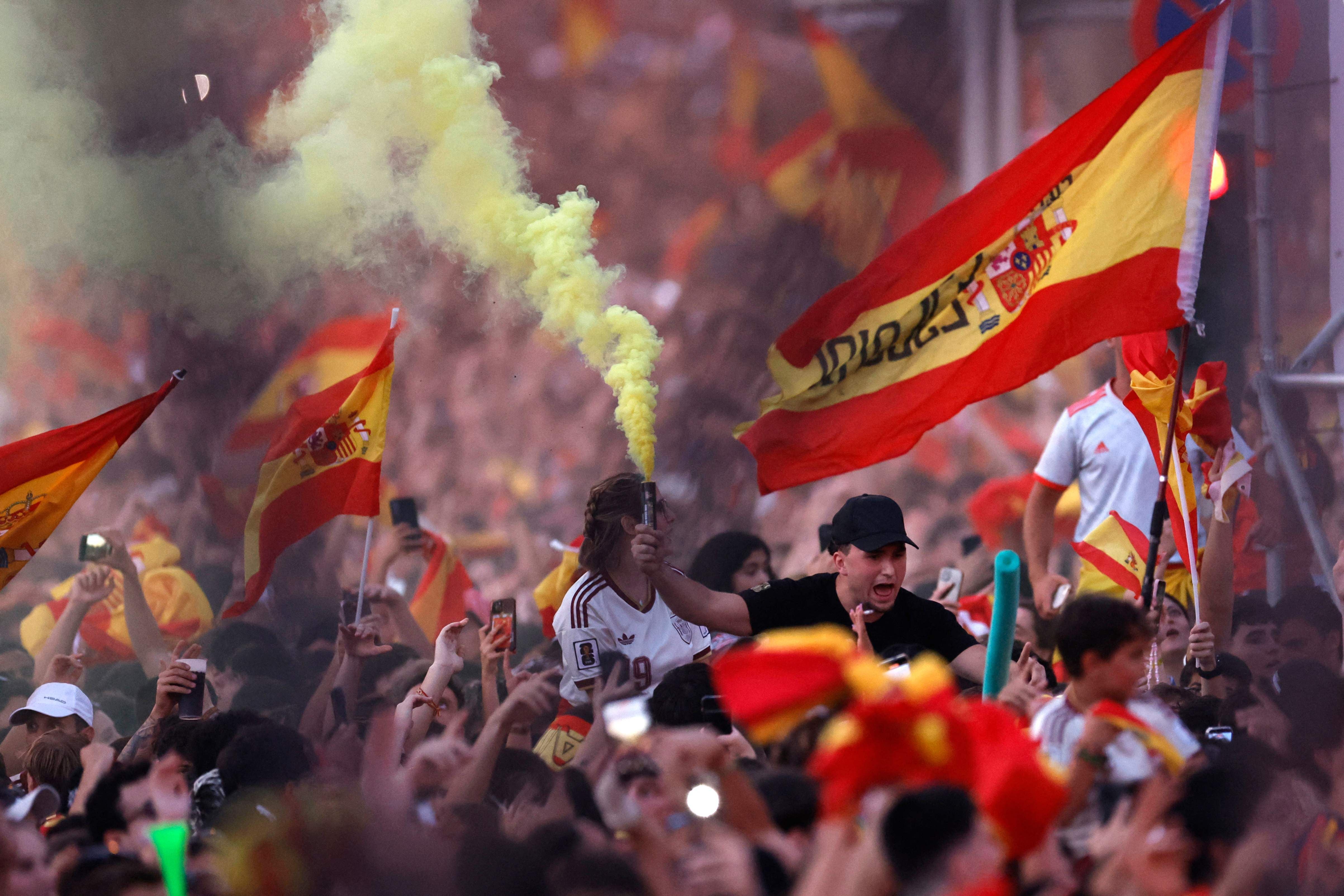 Spanische Fans jubeln mit Fahnen und Rauchfackel auf einem vollen Platz in Madrid.