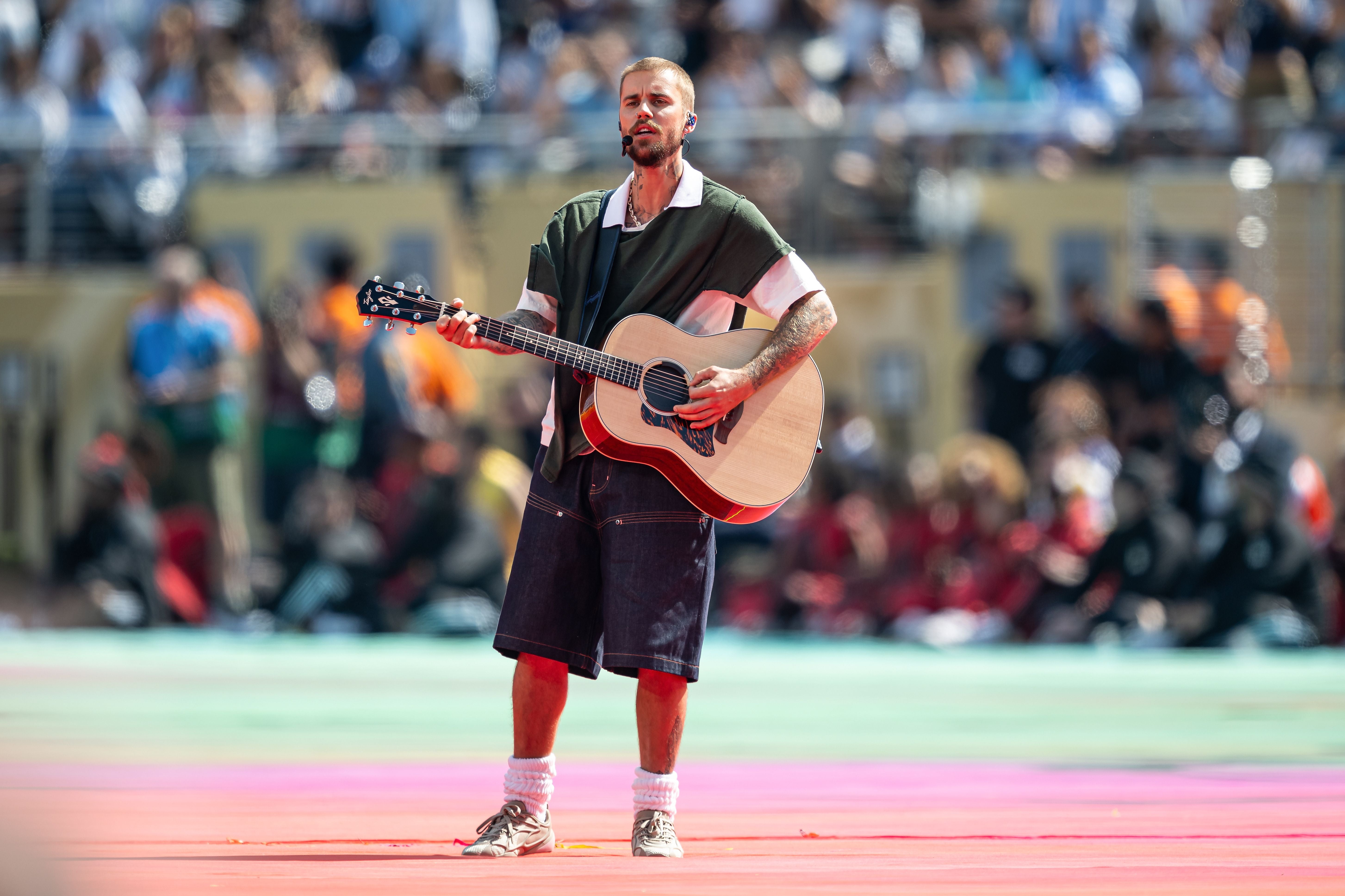 Ein Musiker spielt mit Gitarre auf einer Bühne vor großem, unscharfem Publikum.