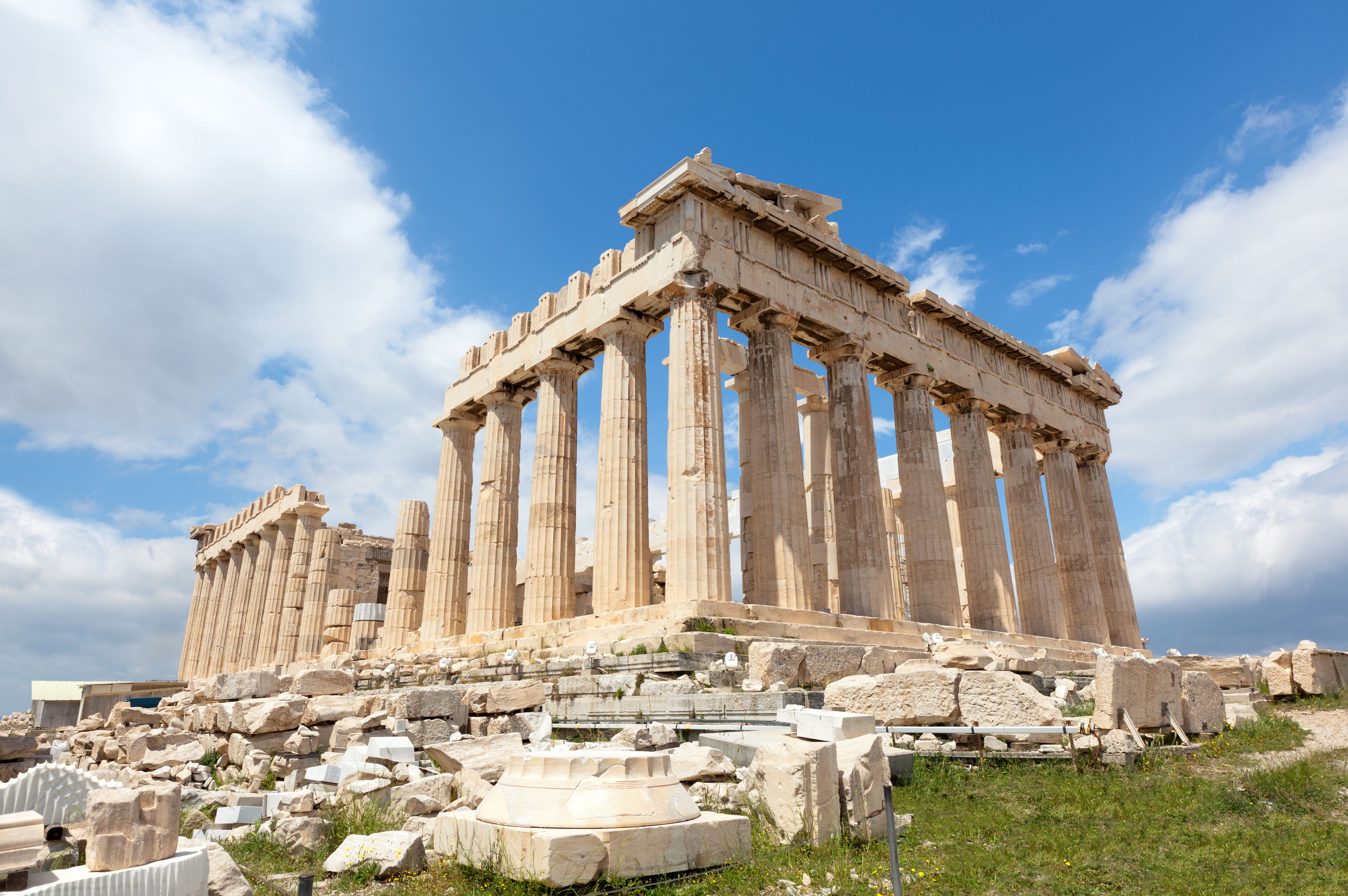 Der Parthenon-Tempel auf der Akropolis in Athen unter blauem Himmel mit verstreuten Ruinen im Vordergrund.