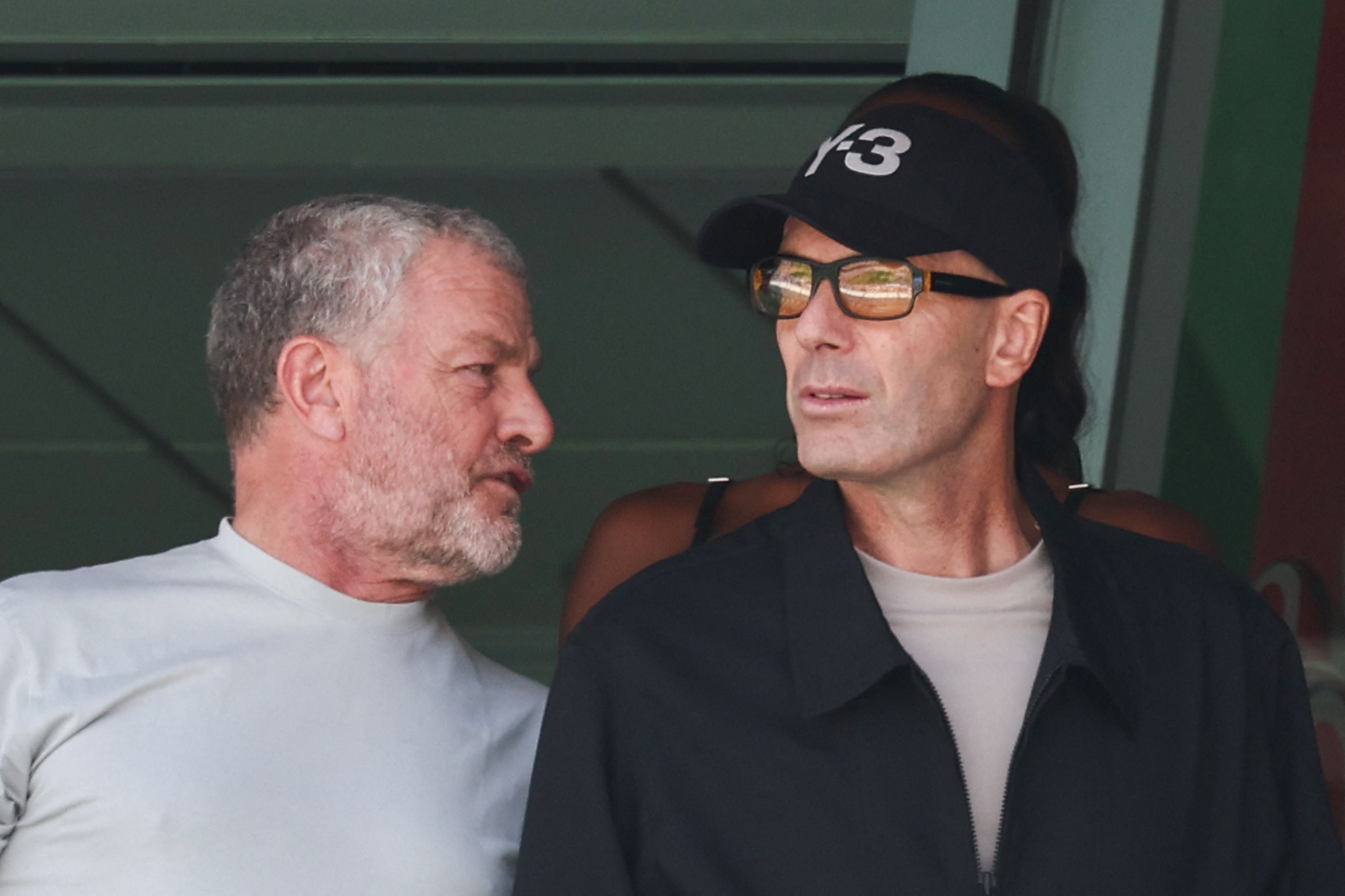 Zwei Männer schauen in unterschiedliche Richtungen und unterhalten sich im Stadion.
