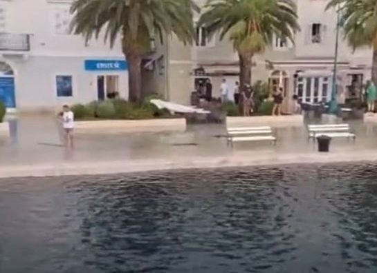 Promenade in Kroatien mit Palmen, Bänken und Menschen am Ufer eines Gewässers.