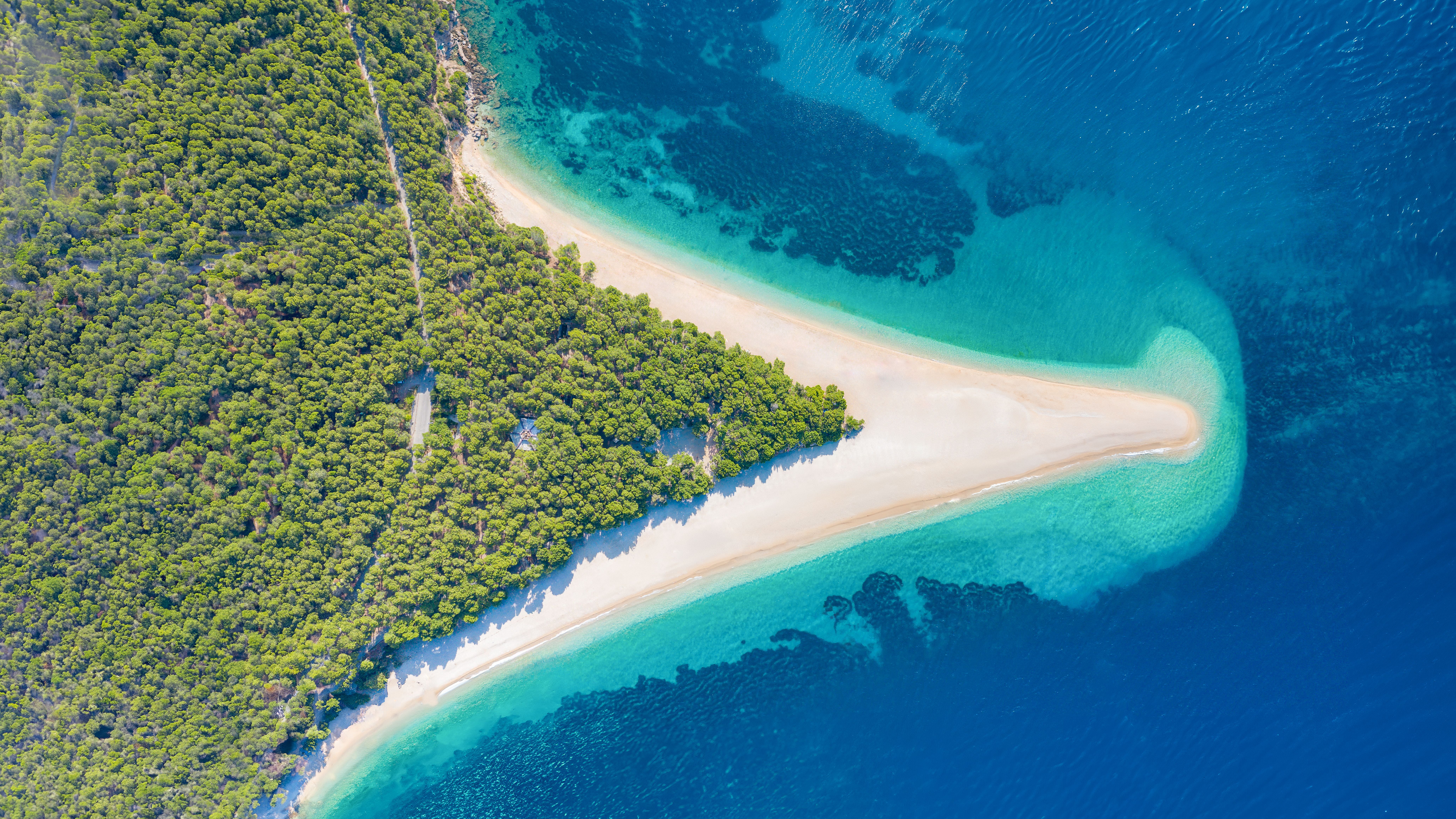 Luftaufnahme des Zlatni Rat Strandes in Kroatien mit türkisfarbenem Wasser und grünem Wald.